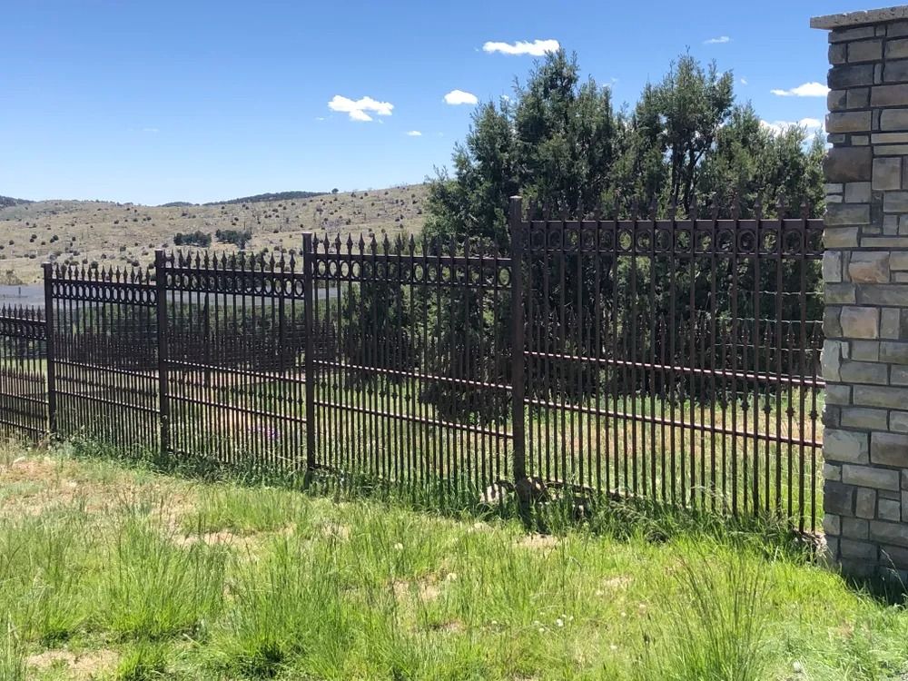 Black metal fence with pointed tops, grassy foreground, and rolling hills in the background.