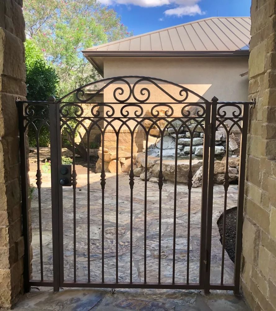 Wrought iron gate with decorative scrollwork between stone columns. Water feature visible beyond the gate.