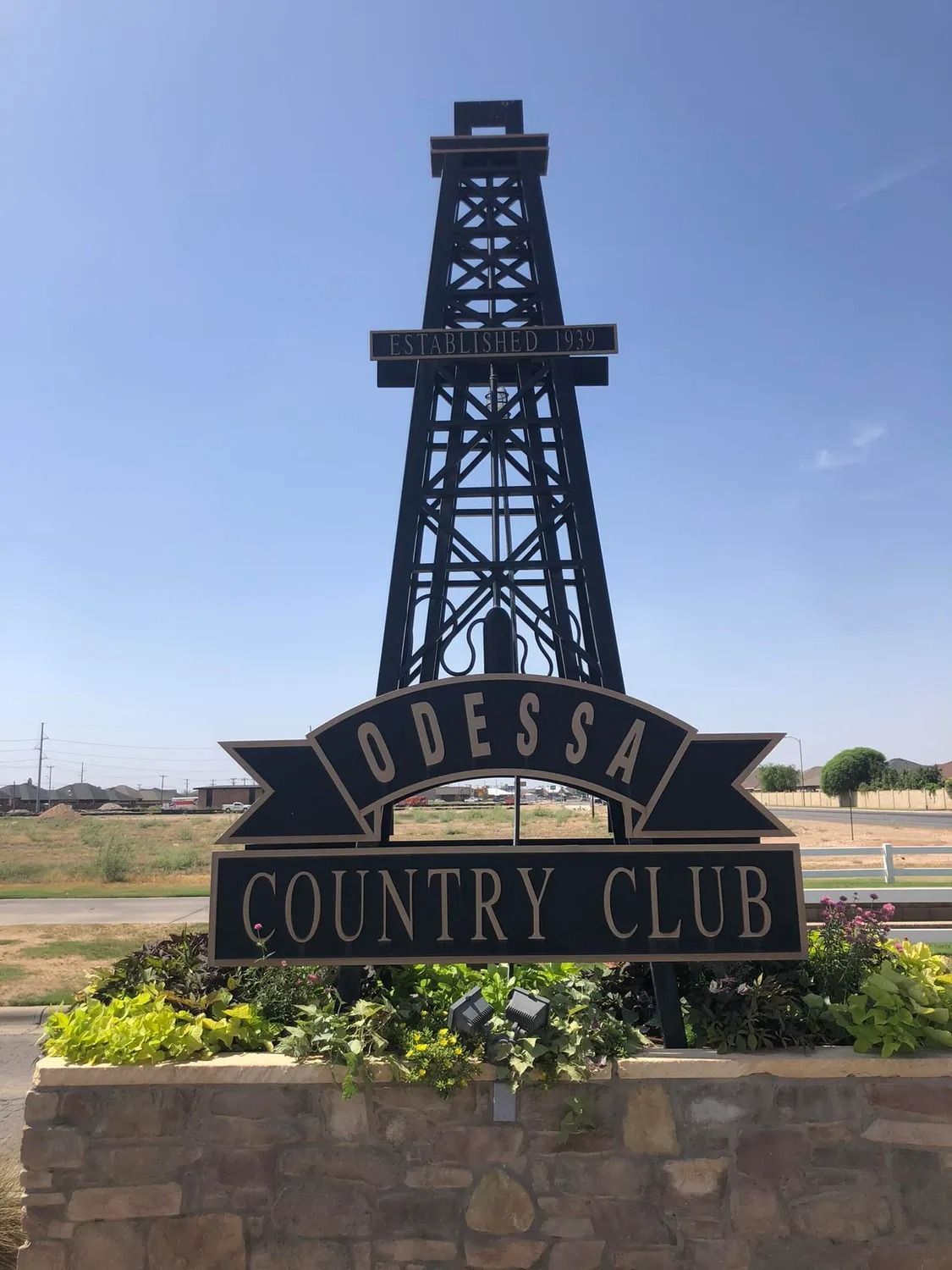 Odessa Country Club sign with oil derrick silhouette, black and gold against a blue sky.