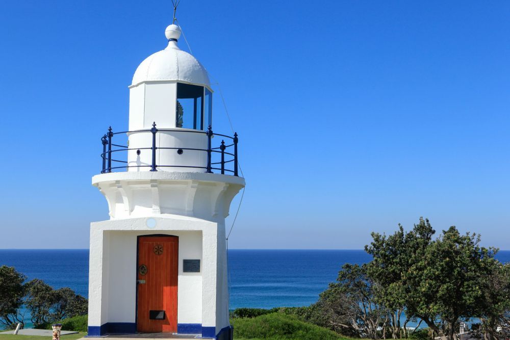 A White Lighthouse With A Red Door Is Sitting On Top Of A Hill Overlooking The Ocean — Tweed Byron Recycling In Ballina, NSW