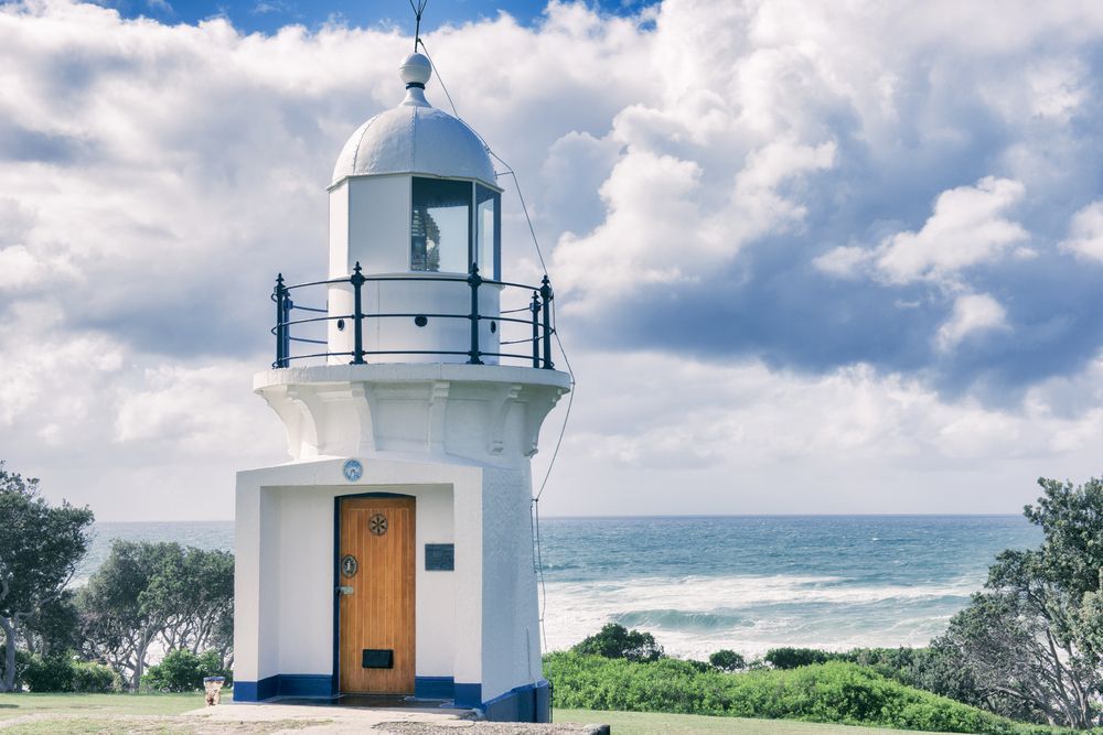 A White Lighthouse With A Wooden Door Is Sitting On Top Of A Hill Overlooking The Ocean — Tweed Byron Recycling In Ballina, NSW