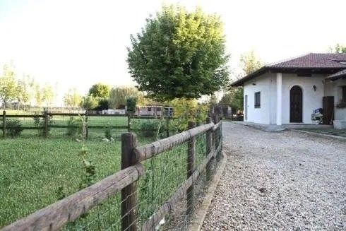Un vialetto di ghiaia conduce a una casa bianca a un solo piano, adiacente a un campo verde recintato da una staccionata di legno.