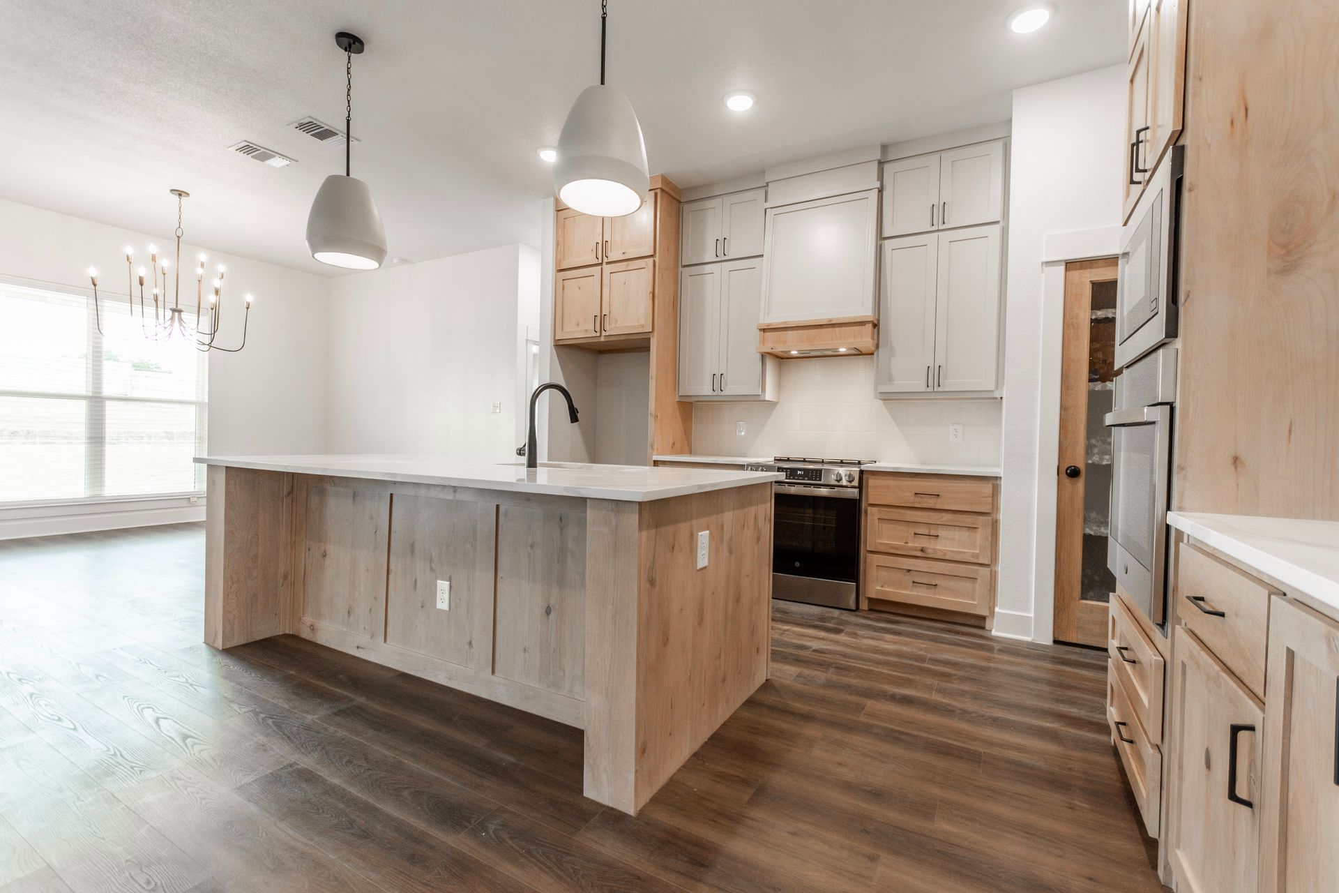 Modern kitchen with light wood accents, white cabinets, and island with pendant lights.
