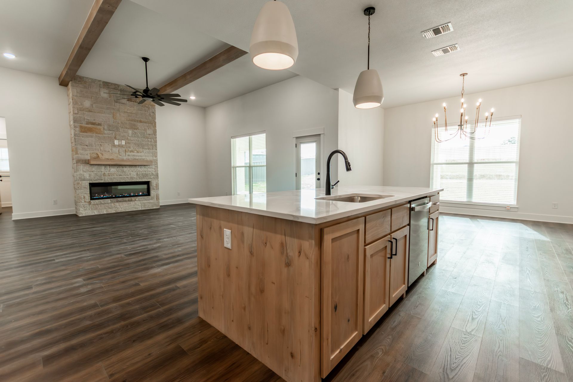 Spacious modern kitchen with island, dark wood floors, fireplace, and light fixtures.