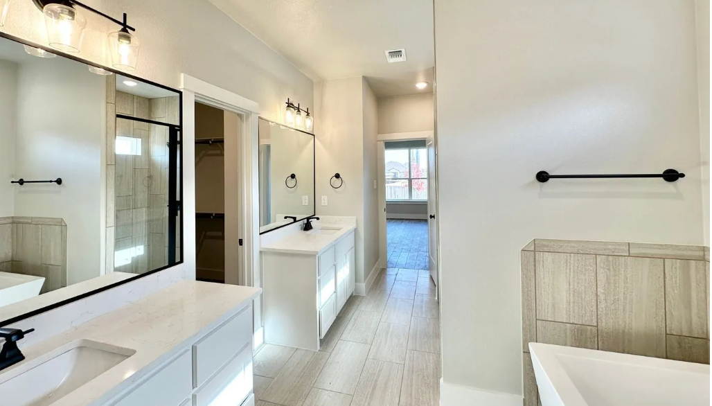 Spacious white bathroom with dual sinks, large mirrors, and a walk-in closet in the background.