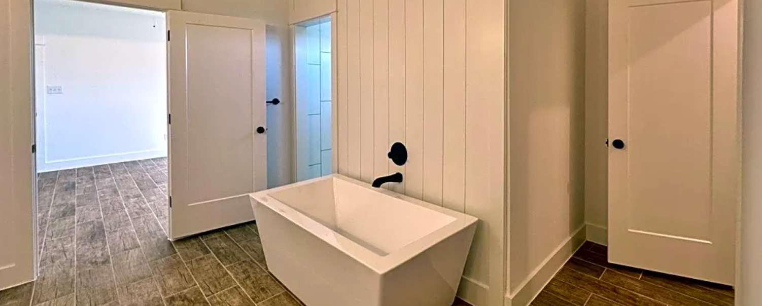 A bathroom with a white freestanding tub, white walls, and wood-look tile flooring.