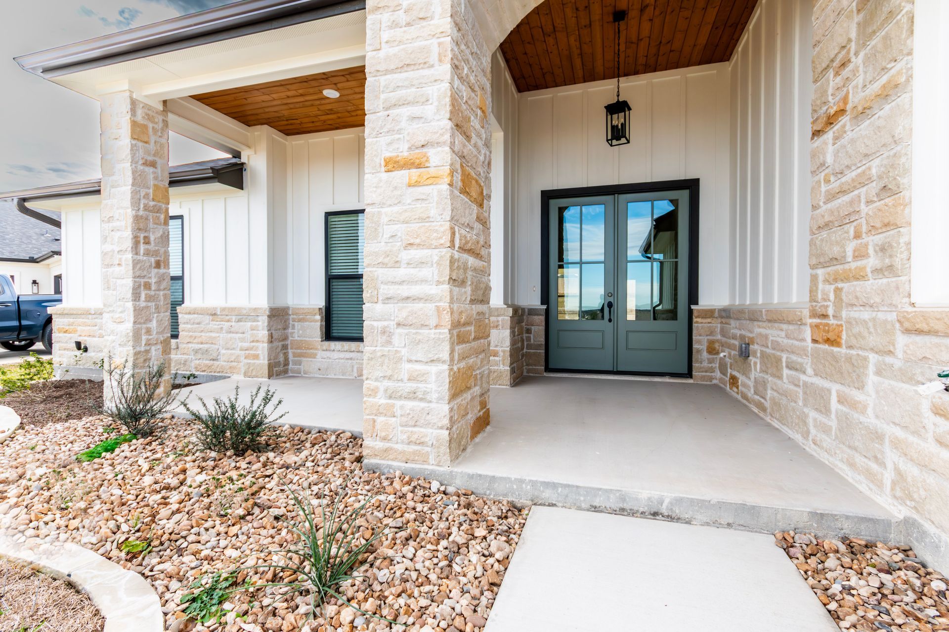 Front porch of a house with stone columns, green double doors, and a gravel yard.