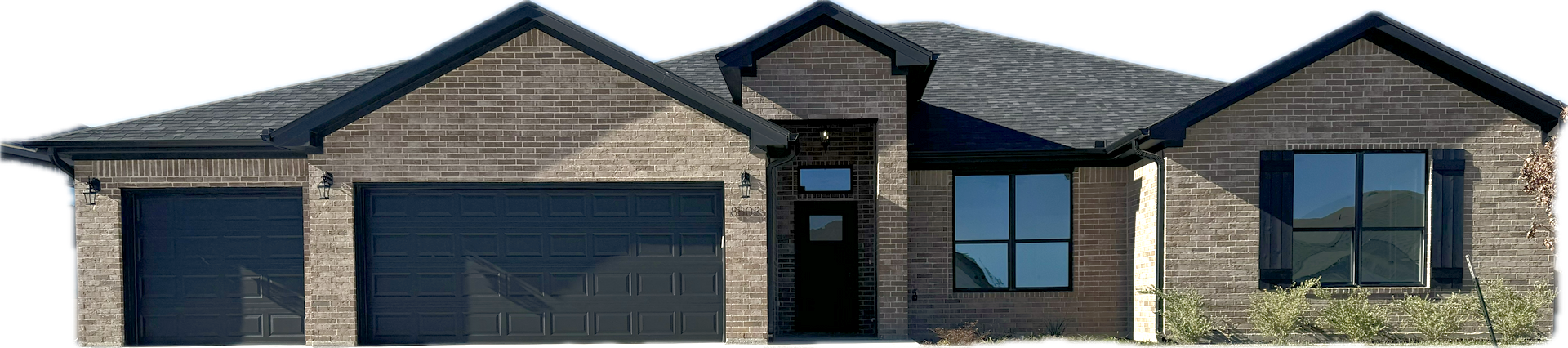 Brick house with dark roof and garage doors, windows.
