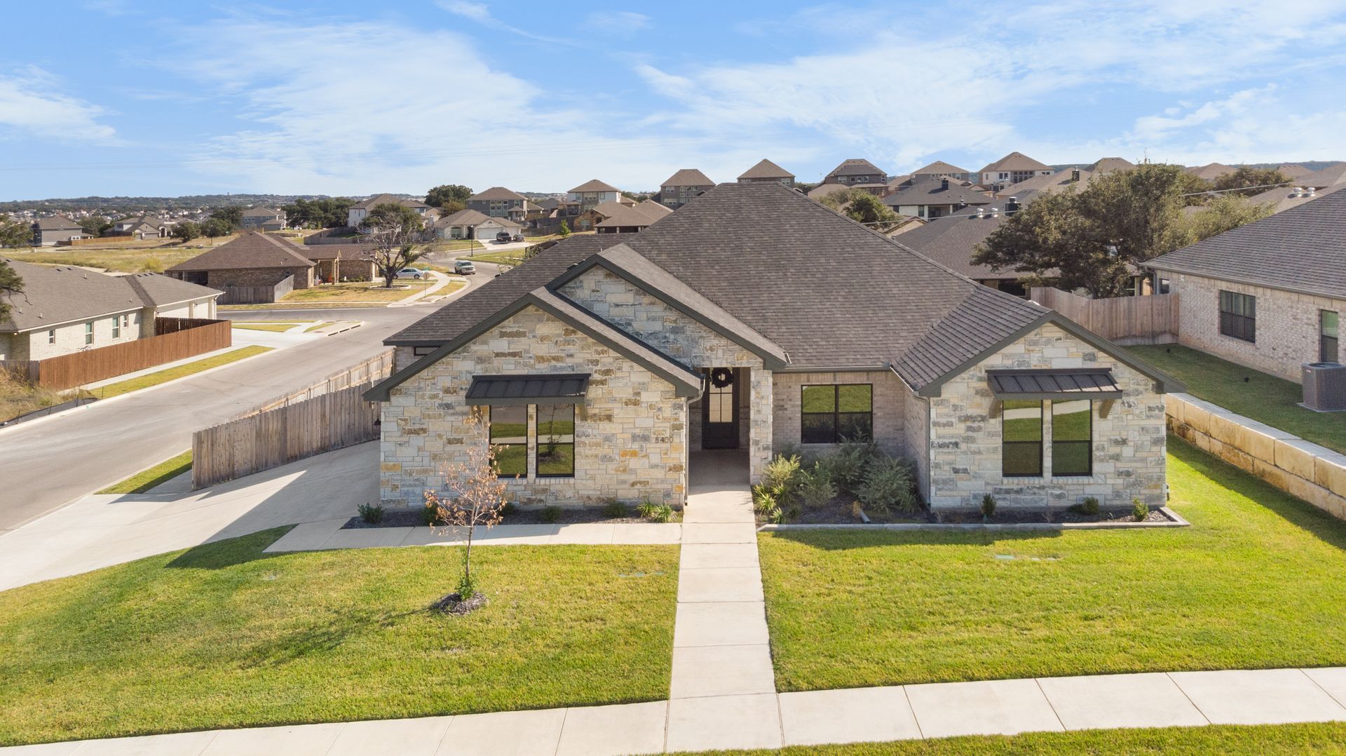 A single-story brick house with a green lawn and blue sky in a suburban neighborhood.