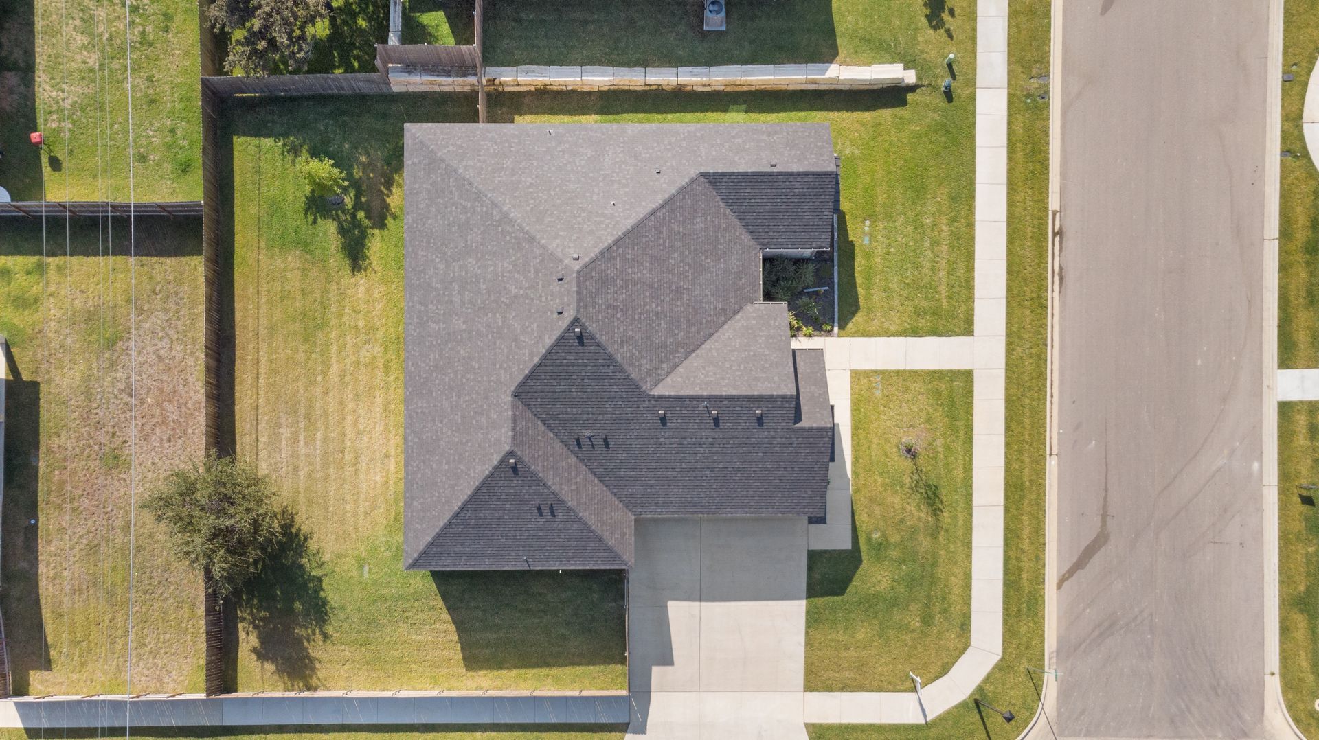 Overhead view of a house with gray roof, green lawn, driveway, and road.