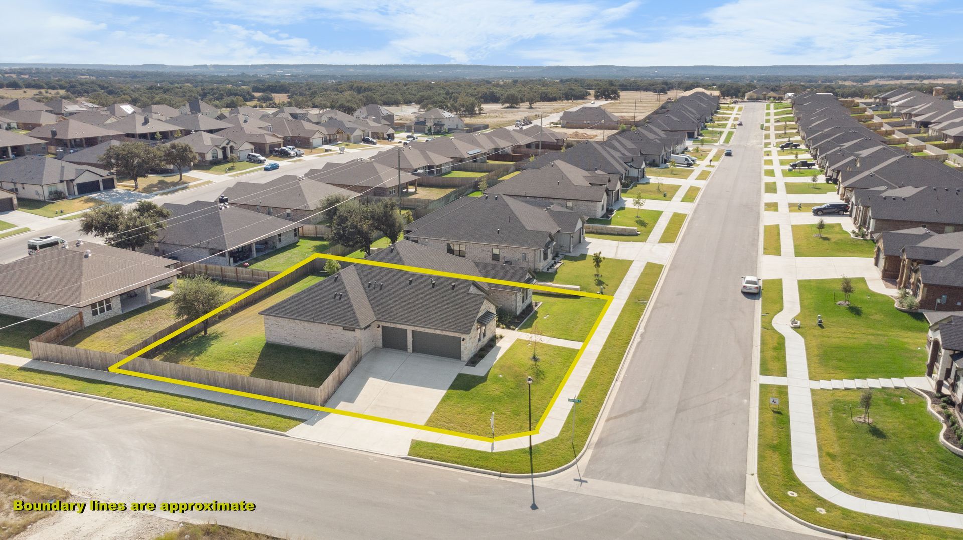 Aerial view of suburban homes on a street corner, outlined in yellow, with green lawns and a clear sky.