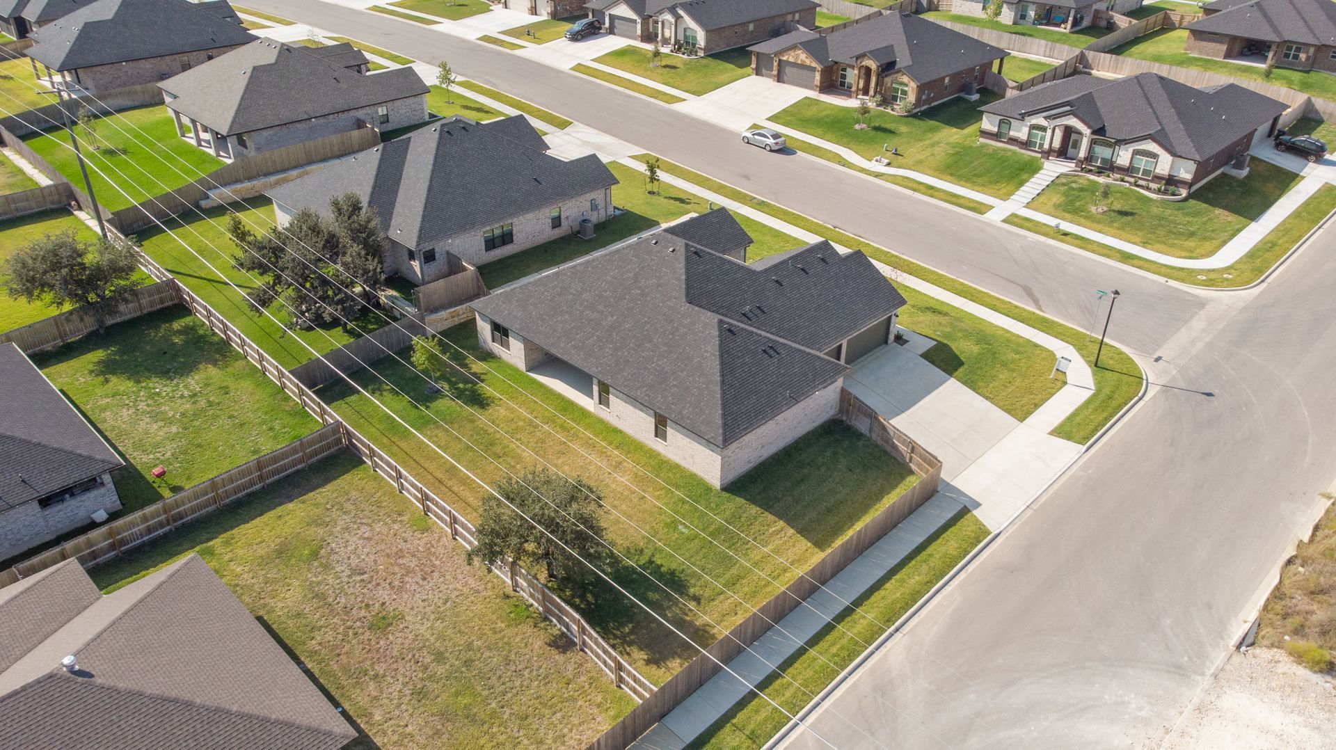 Aerial view of suburban houses with gray roofs, green lawns, and a paved street.