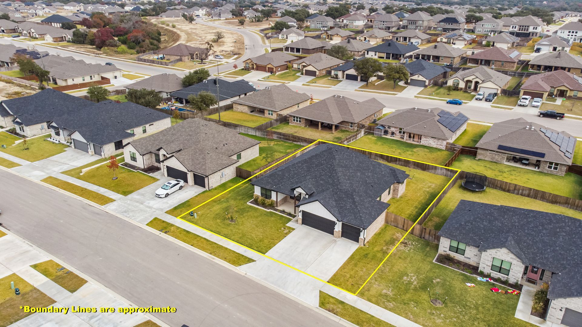 Aerial view of a suburban neighborhood with houses, driveways, and green lawns; cloudy sky.