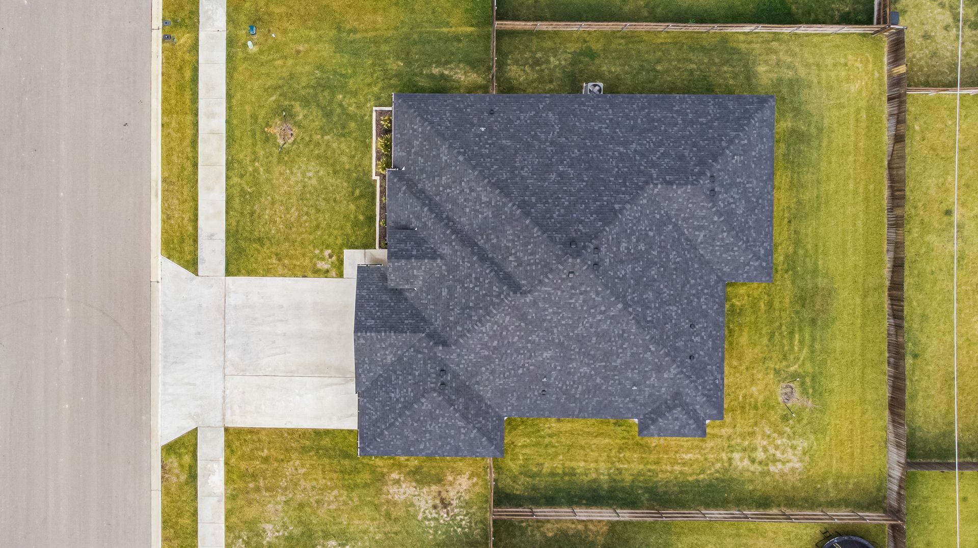Overhead view of a house with a dark roof and concrete driveway, surrounded by green grass.