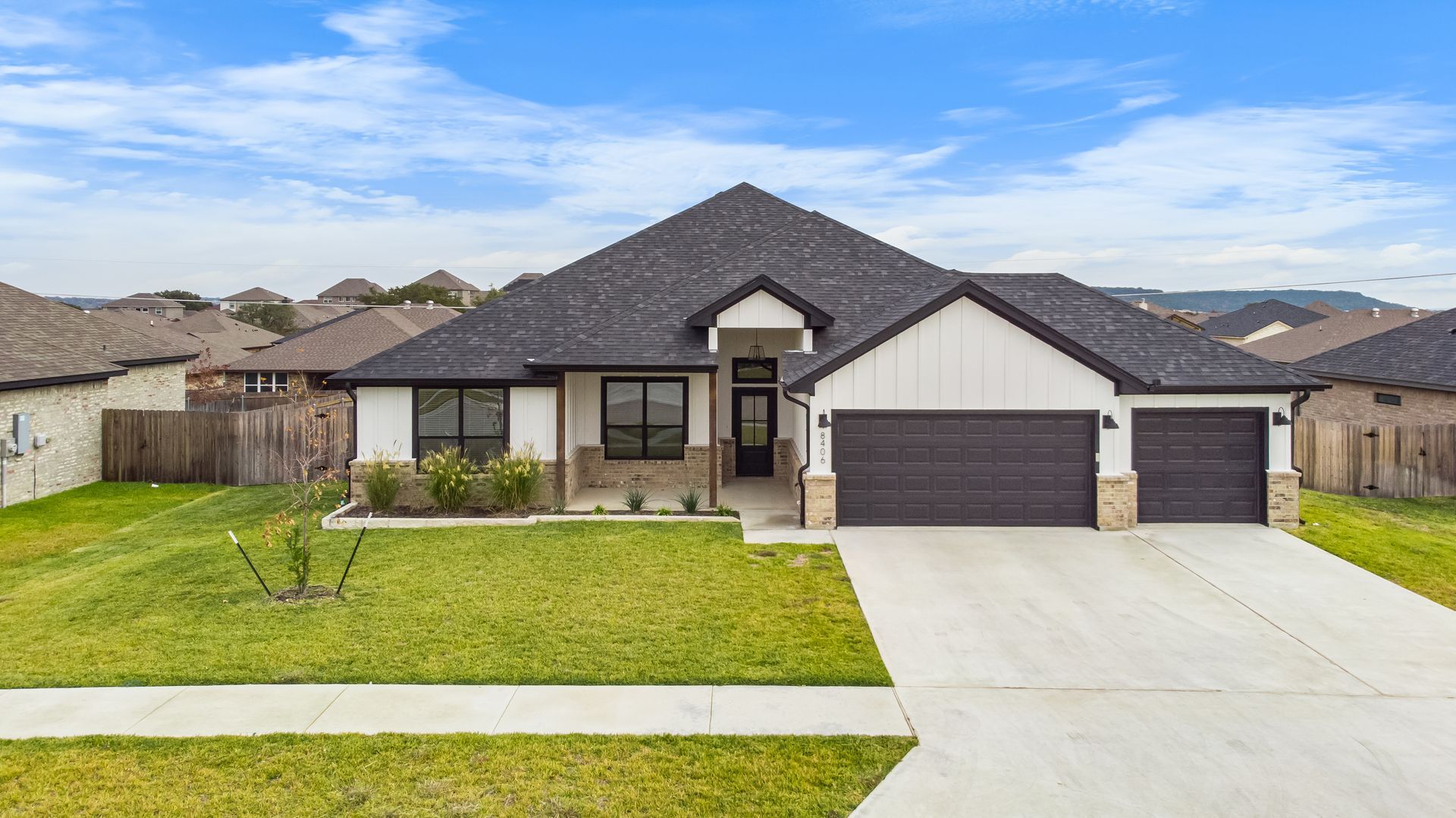 Modern white and black house with a gray roof and attached garage, on a green lawn.