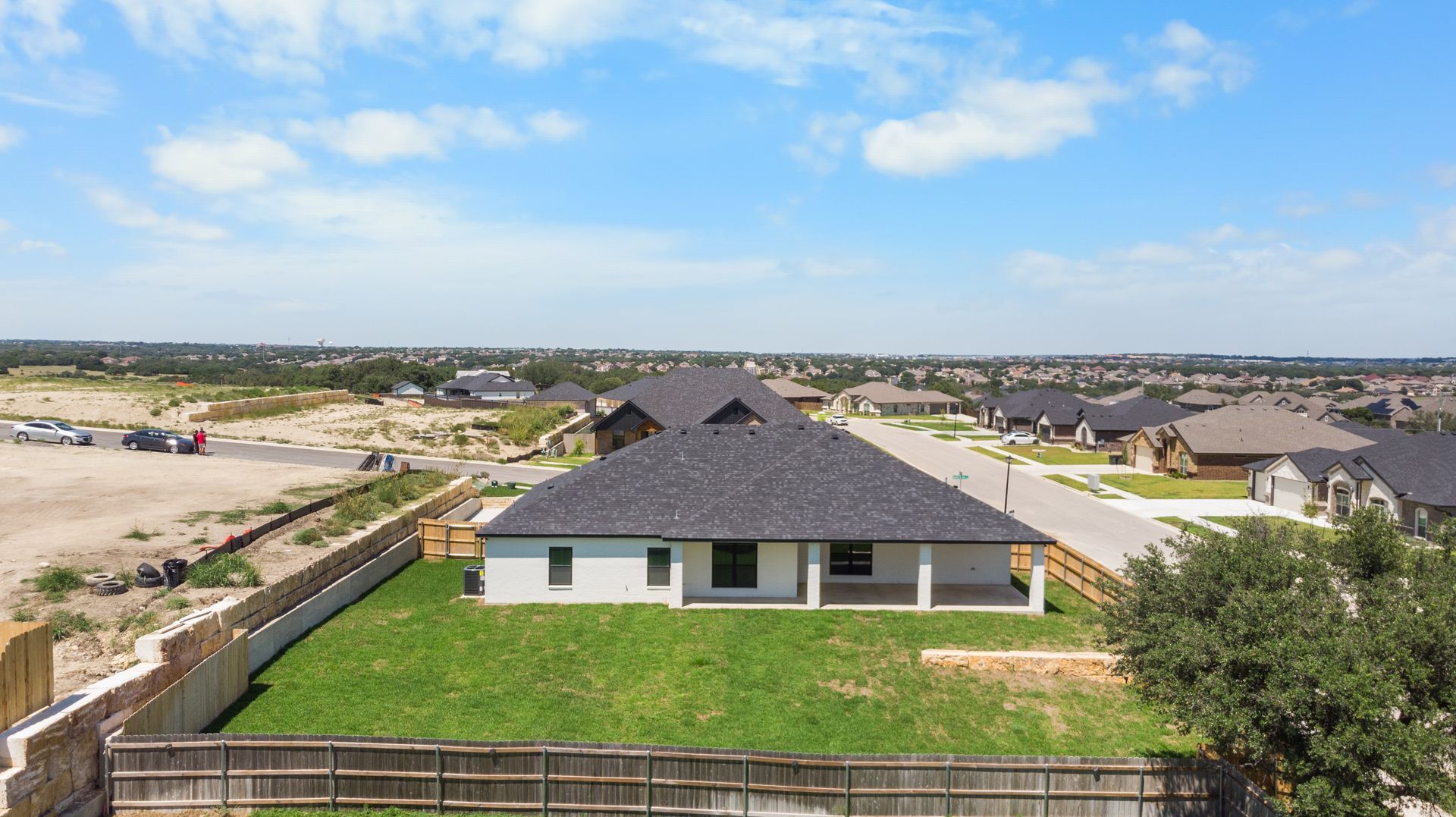 Aerial view of a gray-roofed house with a backyard and surrounding neighborhood on a sunny day.
