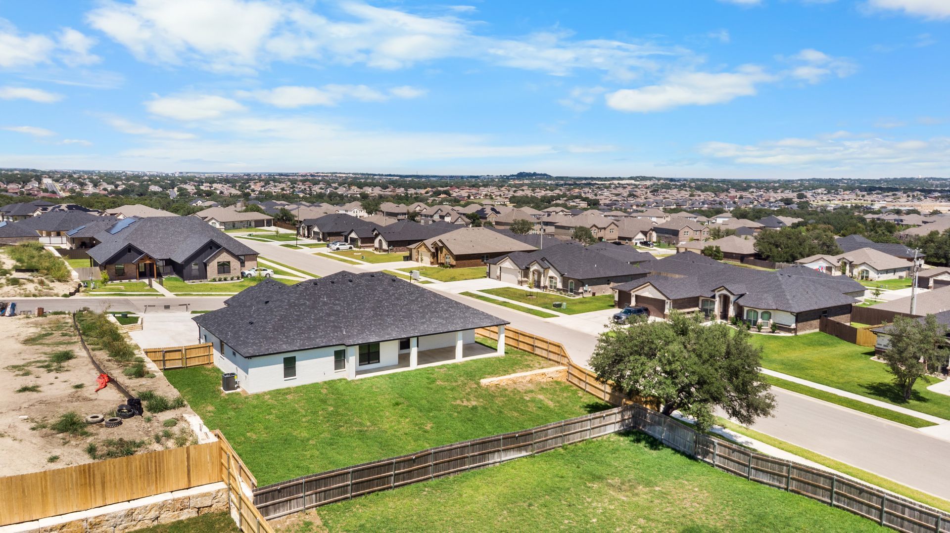 Aerial view of a suburban neighborhood with houses, streets, and green lawns under a blue sky.