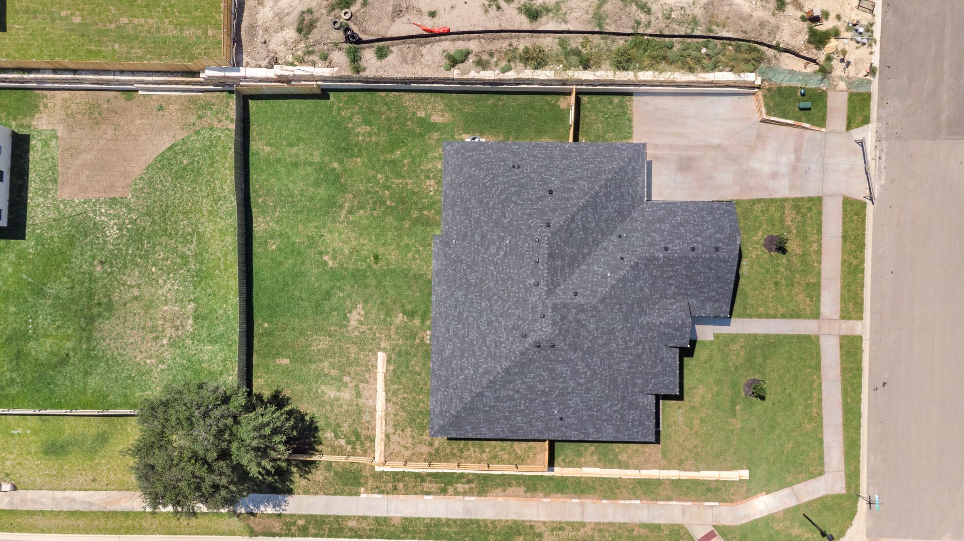 Overhead view of a house with dark gray roof, surrounded by grass and sidewalk.