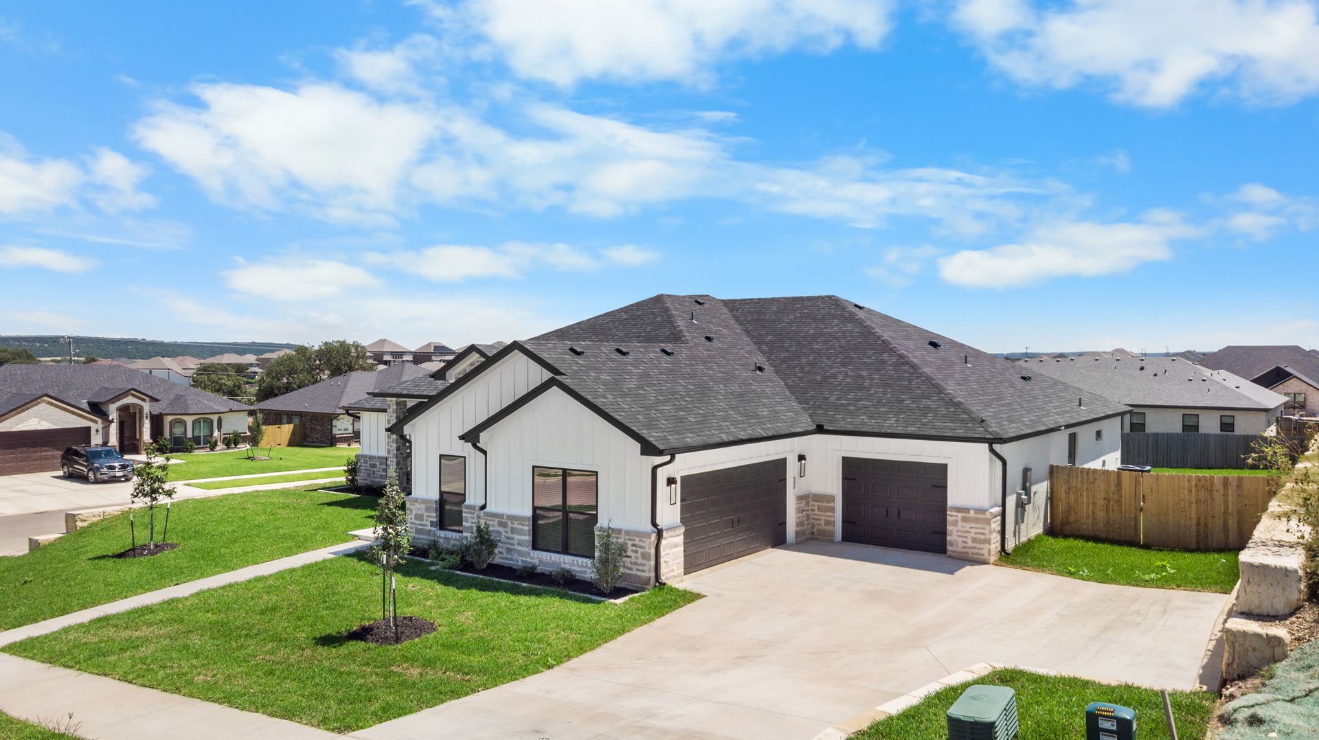 Modern white house with dark roof, two-car garage, and manicured lawn under a blue sky.