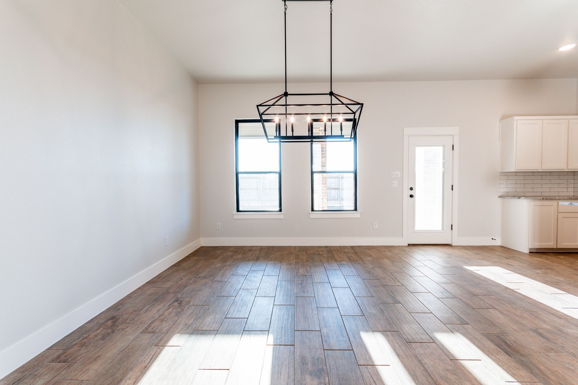 Empty dining room with wood floors, windows, and a modern chandelier.