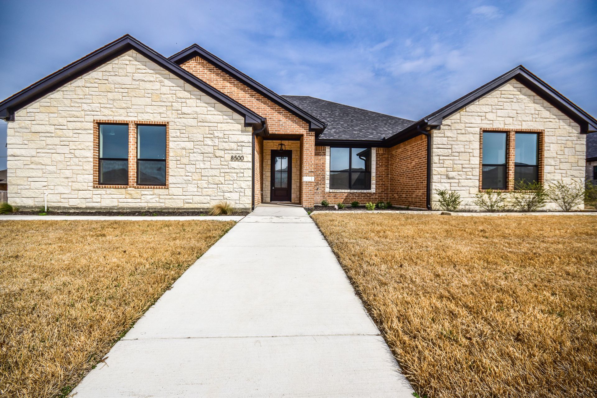 A tan brick house with a white walkway, brown accents, and a blue sky.