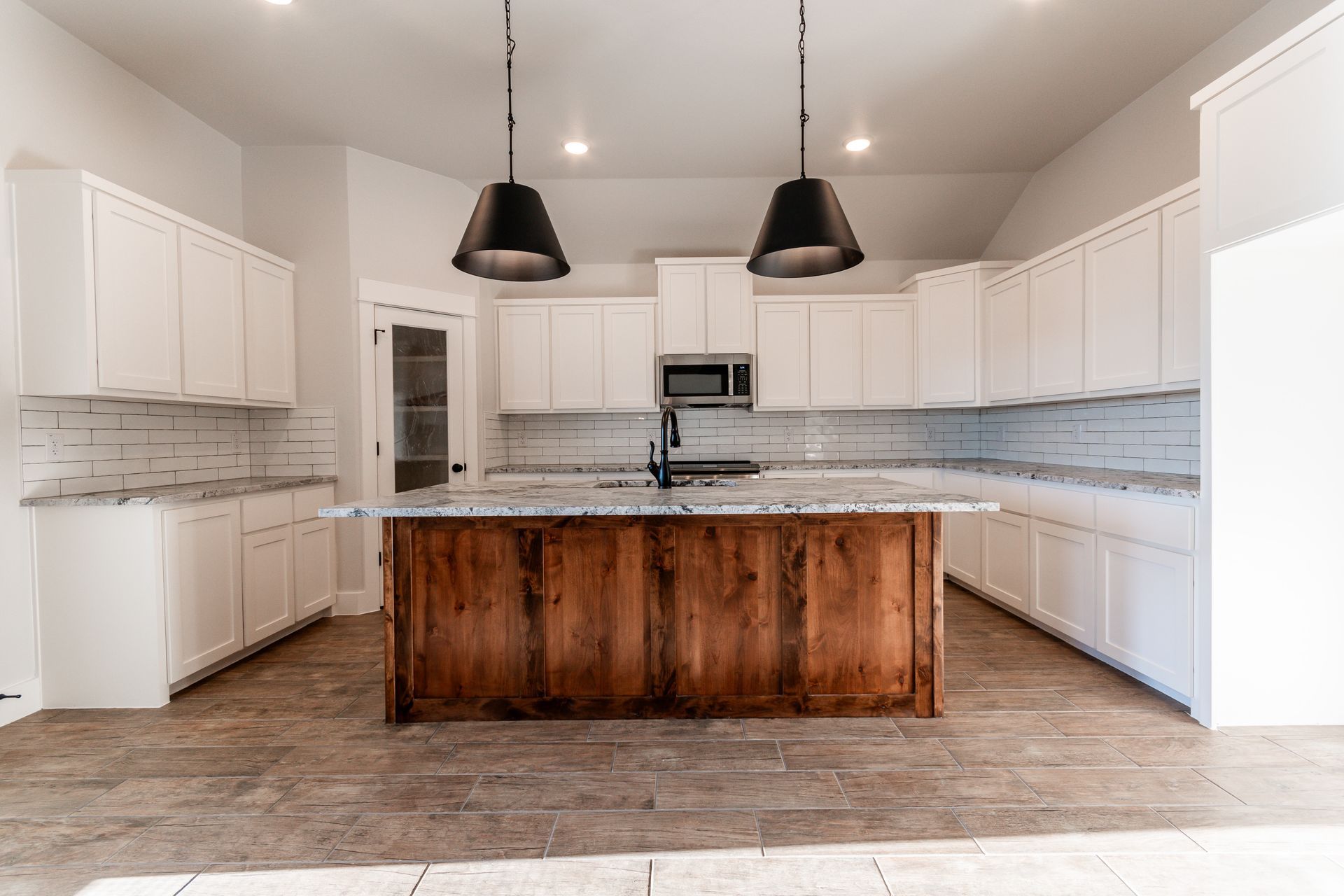 Modern kitchen with white cabinets, wood island, and black pendant lights.