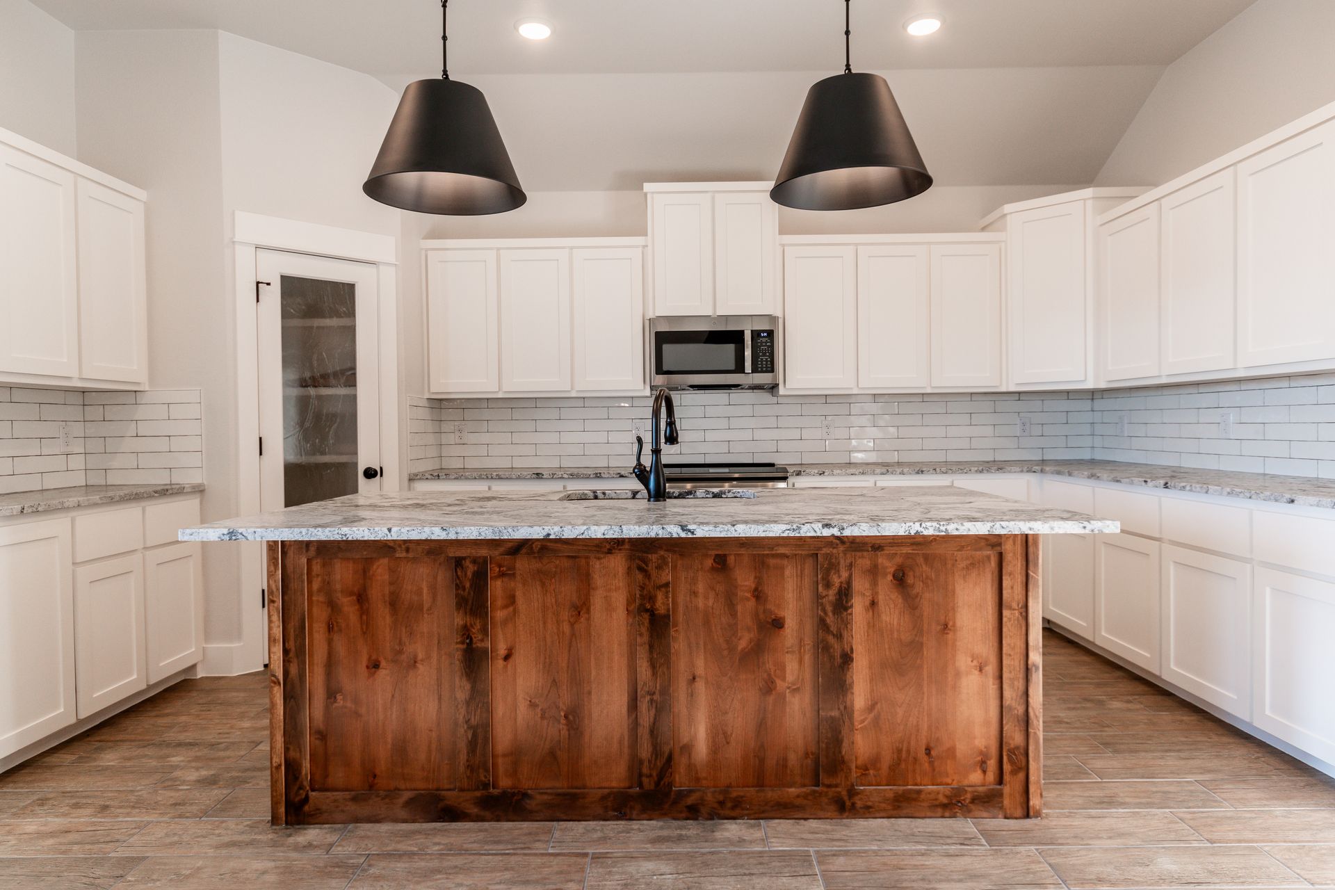 Modern kitchen with white cabinets, wood island, and black pendant lights.