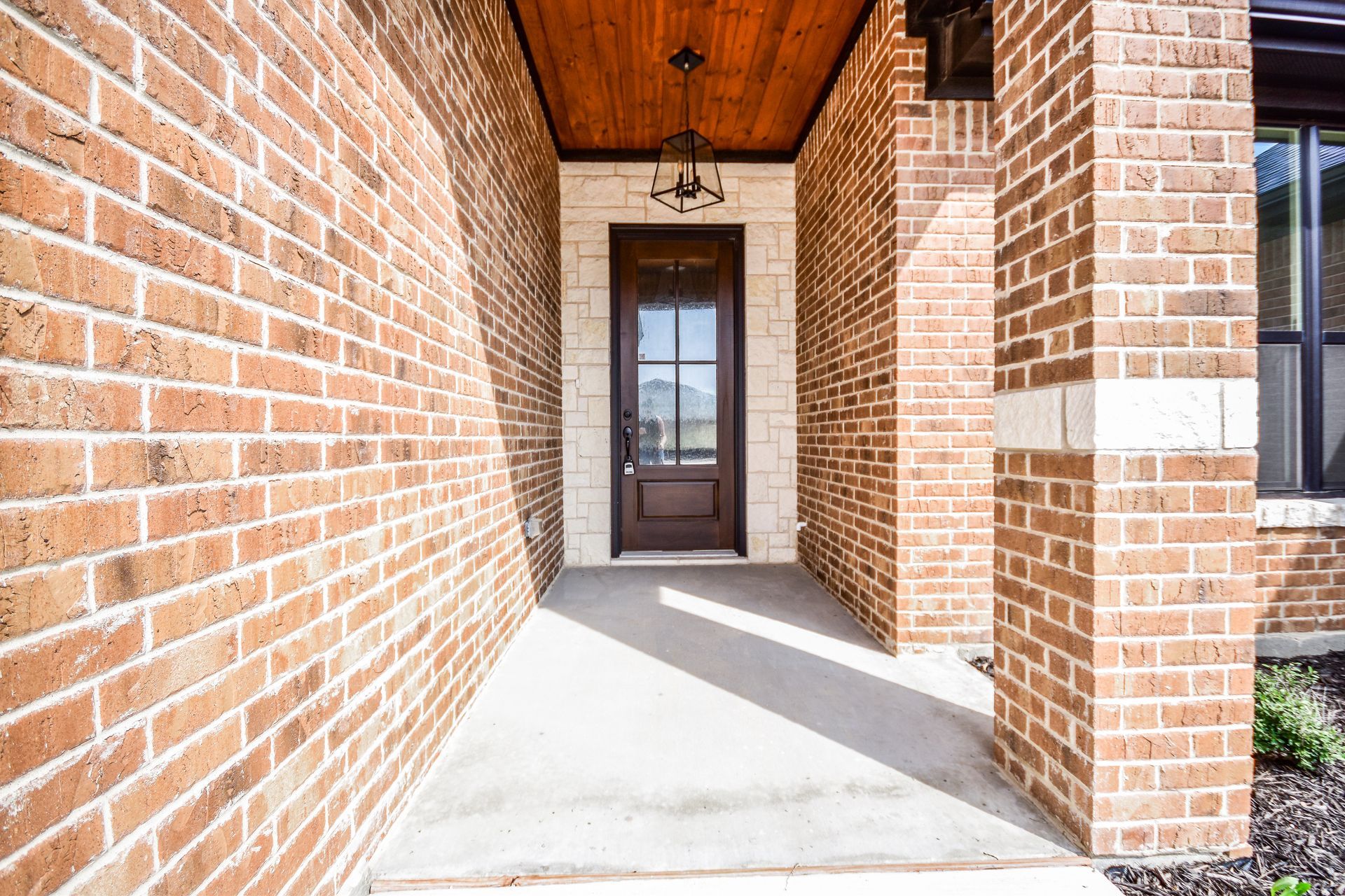 Brick entryway with a dark brown door, concrete floor, and wood ceiling.