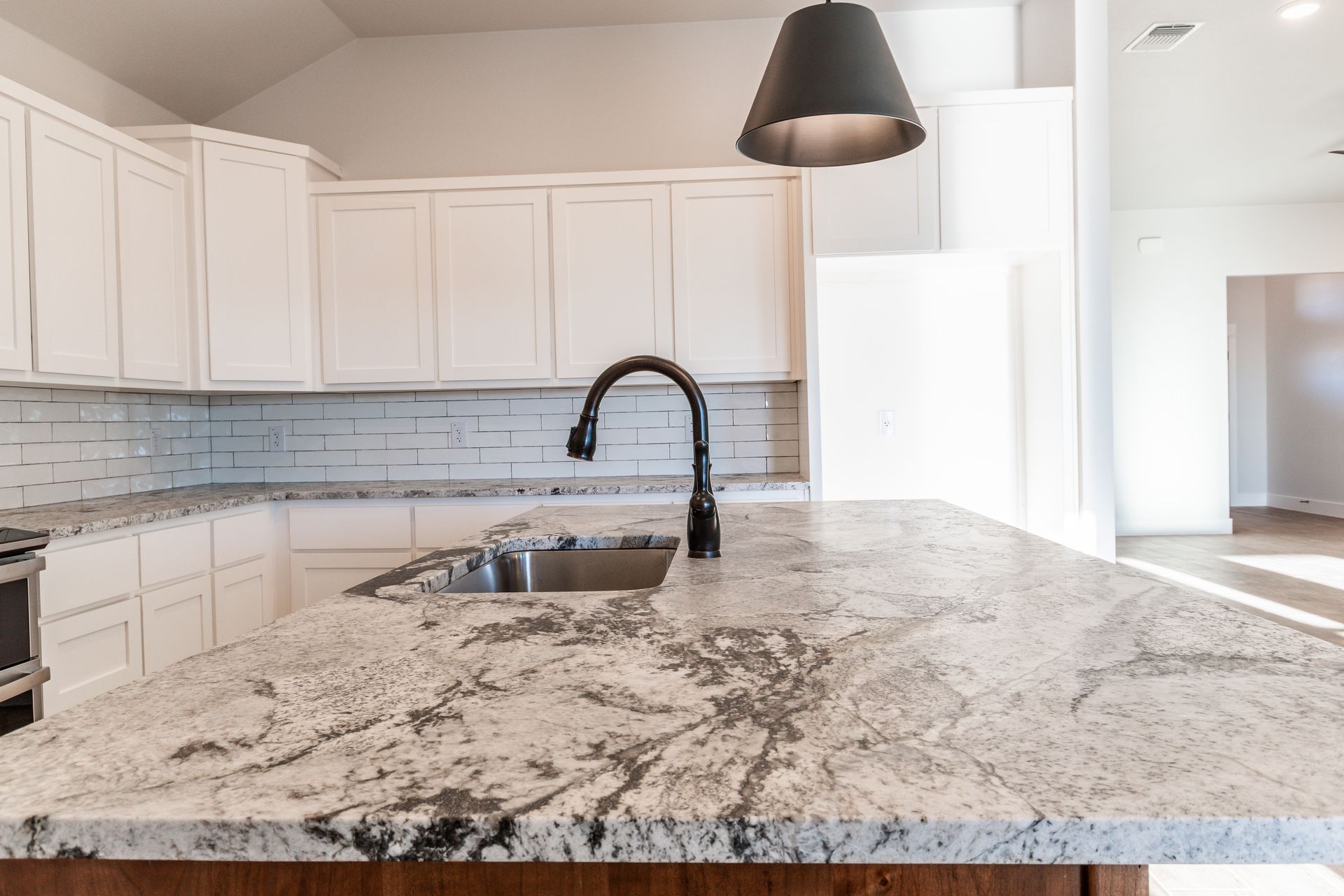 Kitchen with white cabinets, granite countertop, black faucet, and pendant light.