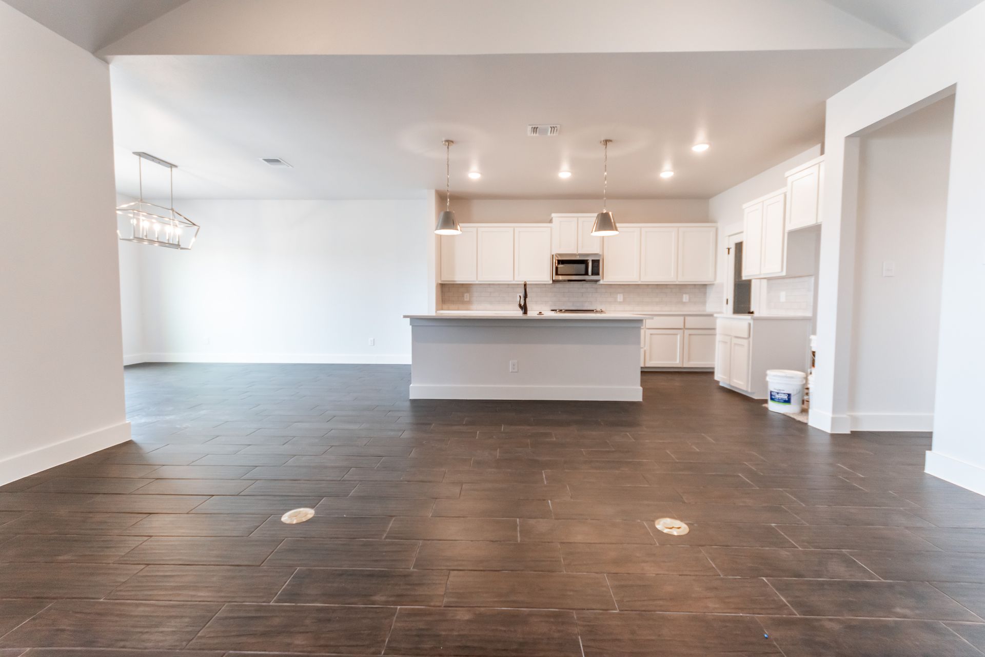 Open-concept kitchen and living area with white cabinets, island, dark wood floors, and recessed lighting.