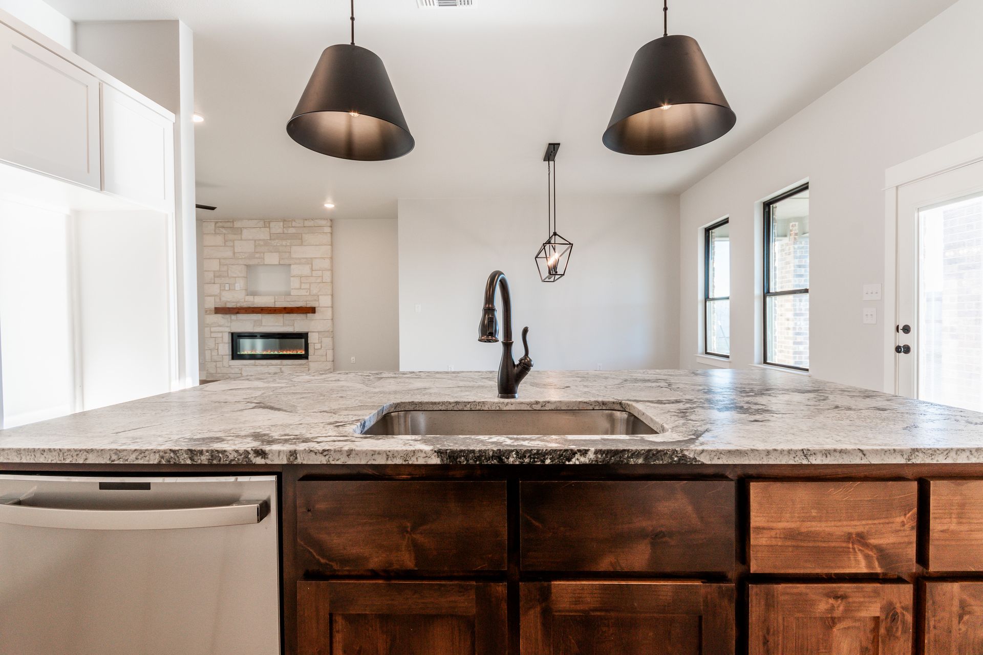 Kitchen with granite countertop, dark wood cabinets, black faucet, and pendant lights. A fireplace is in the background.