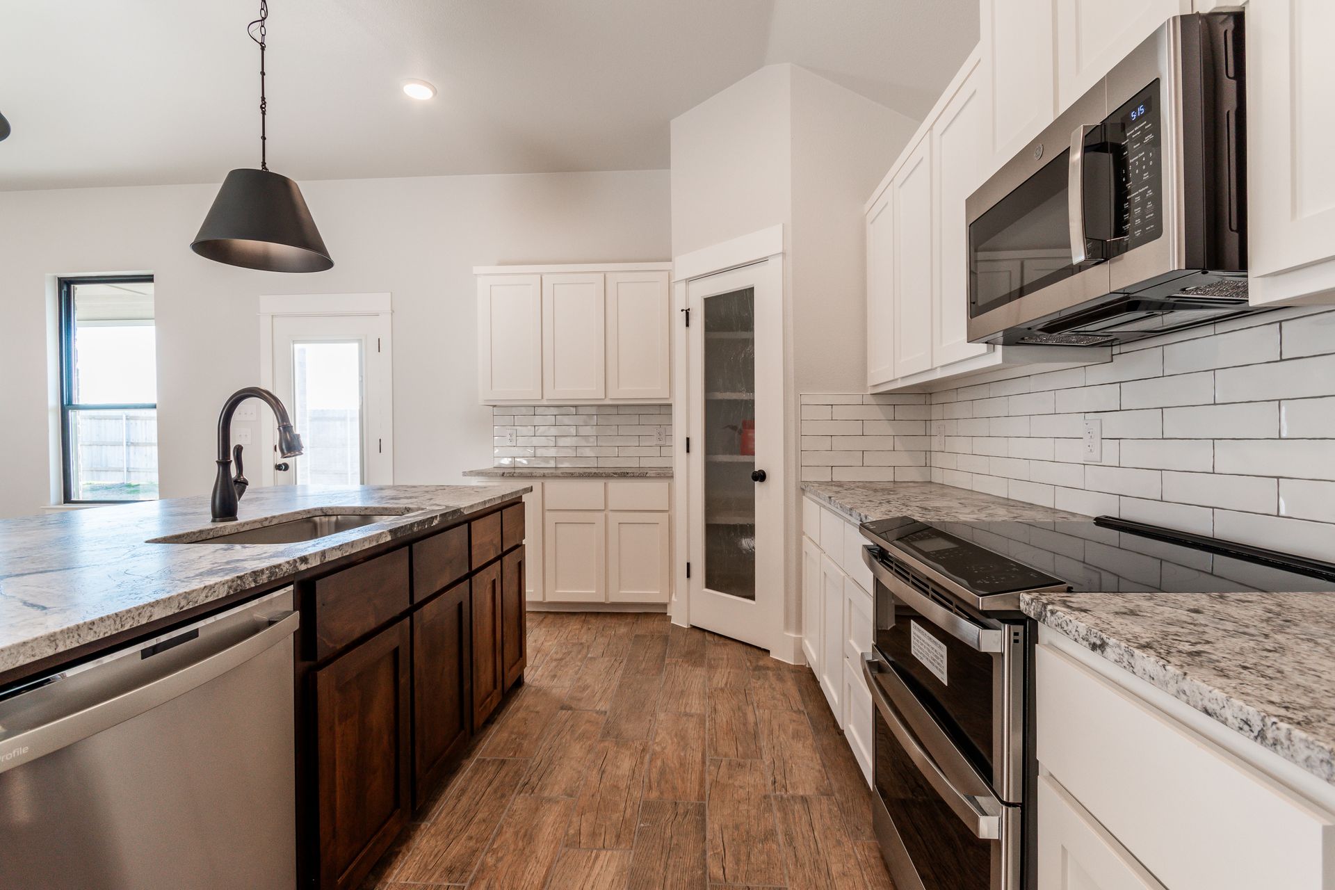 Modern kitchen with white cabinets, dark island, stainless steel appliances, and wood floors.
