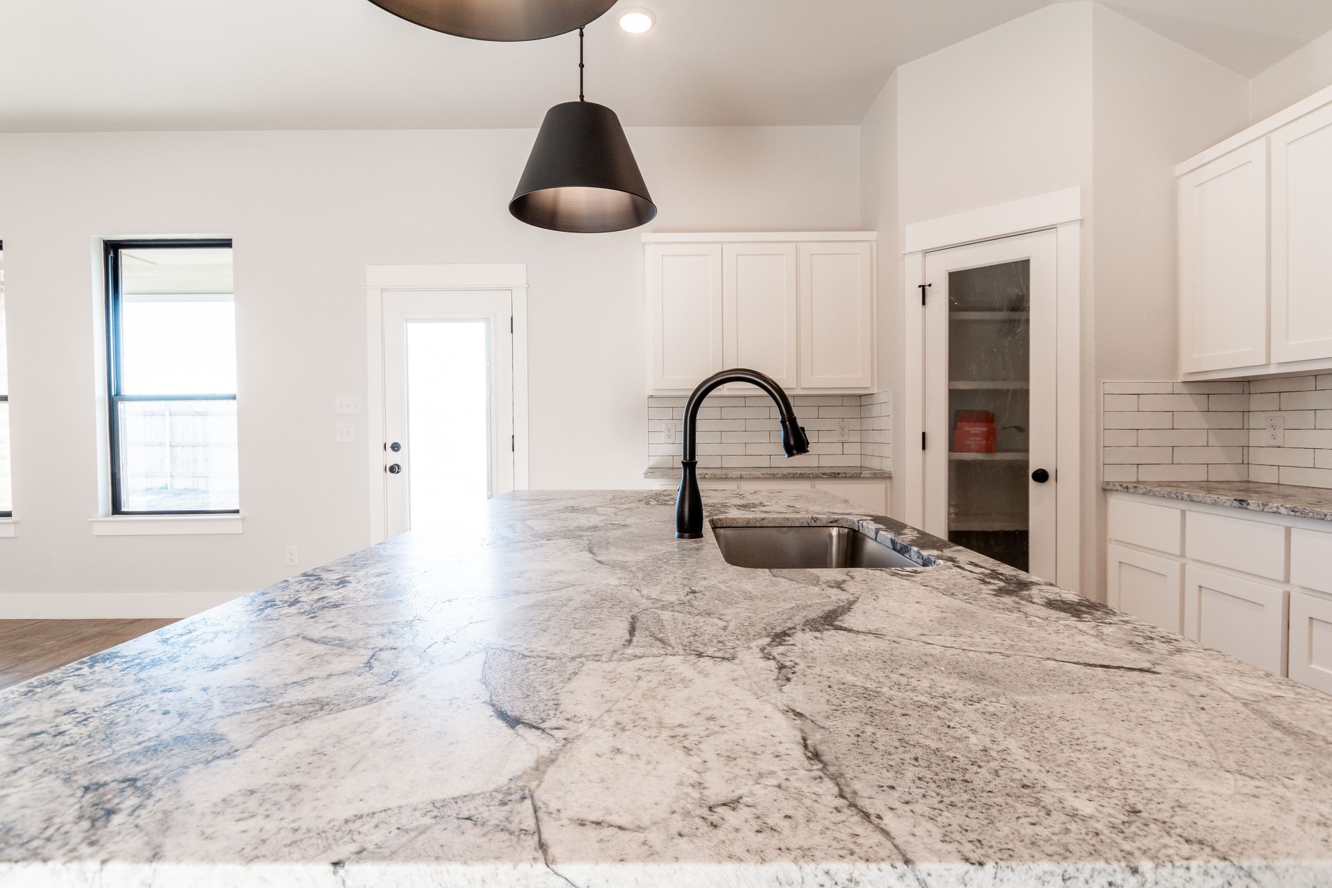 Kitchen with granite countertop island, black faucet, white cabinets, pendant light.