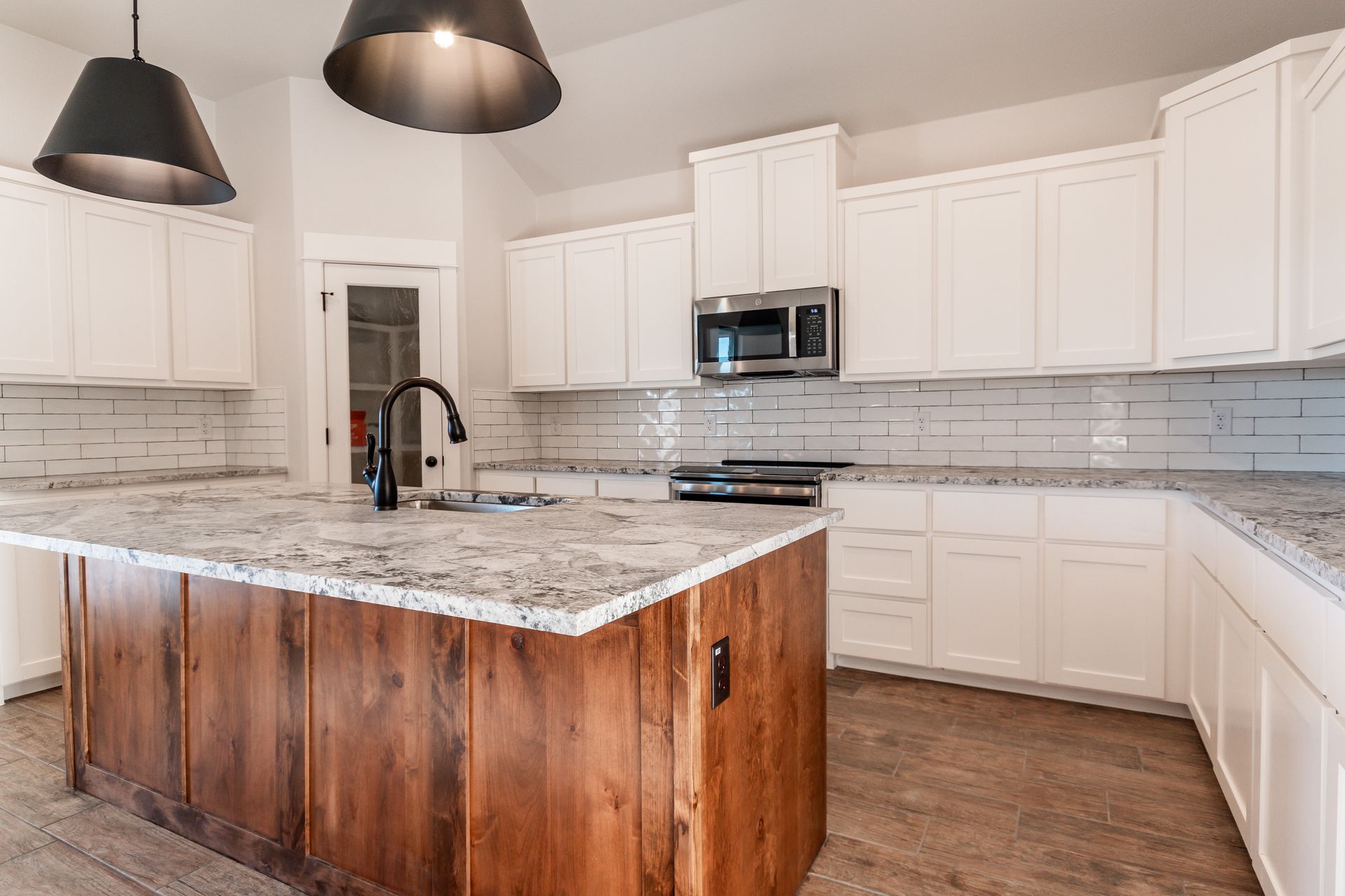 Kitchen with white cabinets, wood island, granite countertops, and black fixtures.