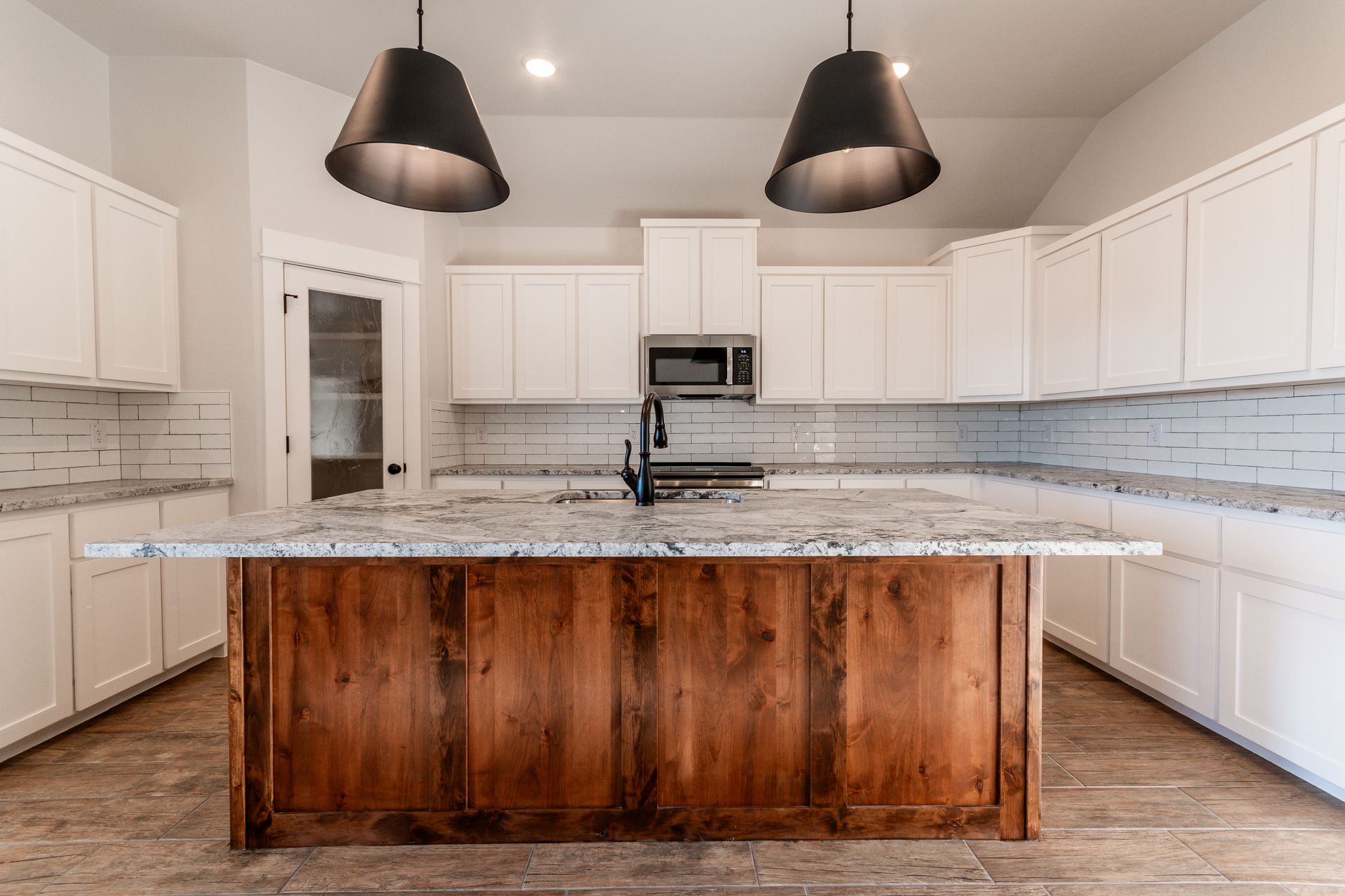 Kitchen with white cabinets, wood island, granite countertops, and black pendant lights.