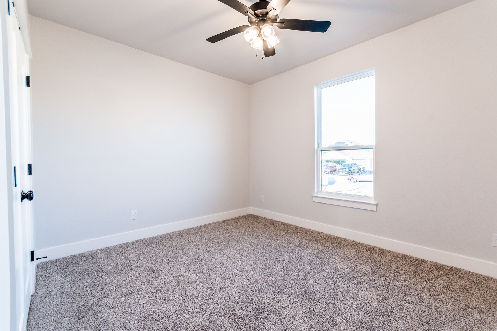 Empty bedroom with beige carpet, window, ceiling fan, and white walls.