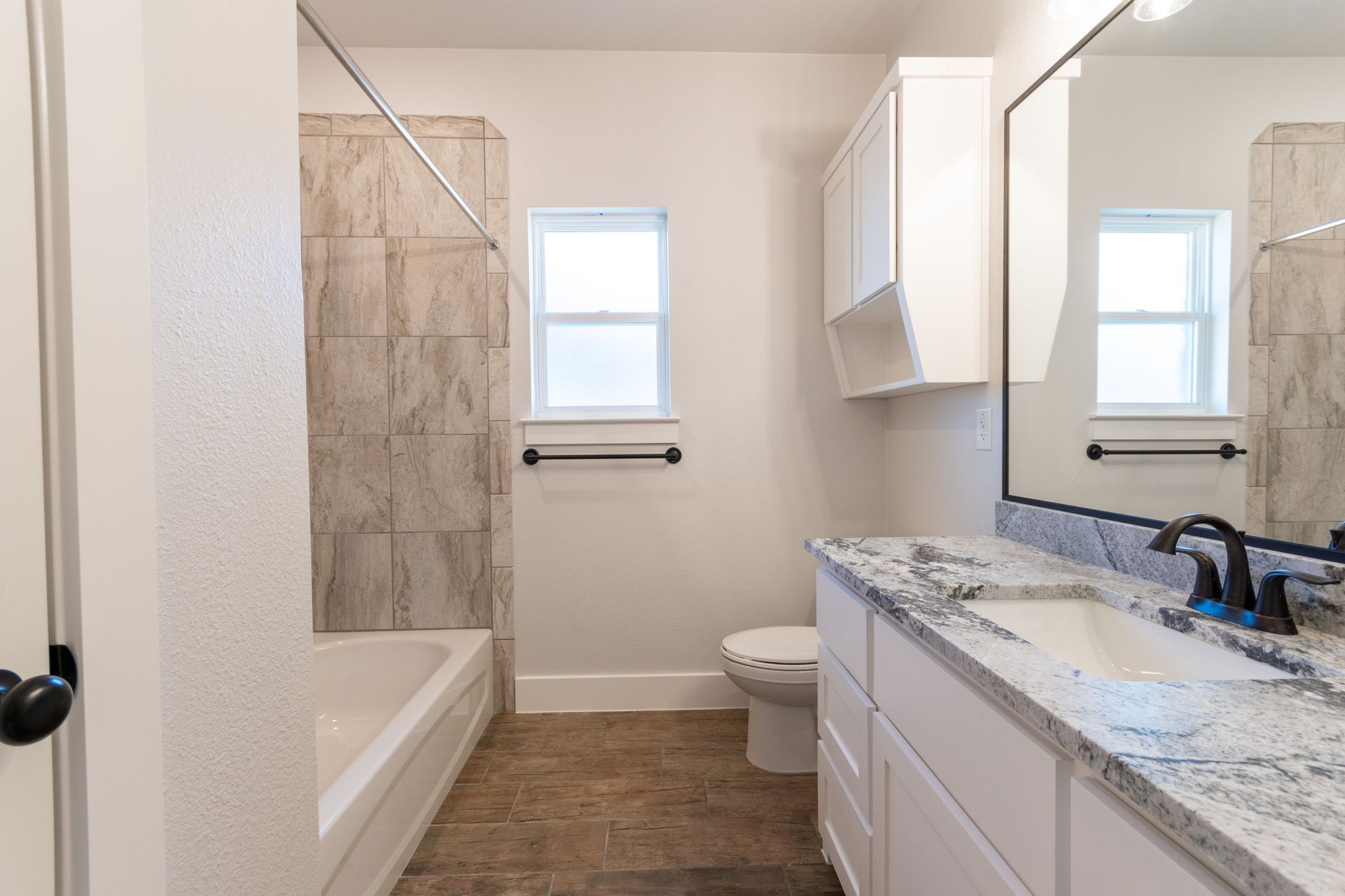 Bathroom with a tub/shower combo, vanity, toilet, and window, all in neutral tones.