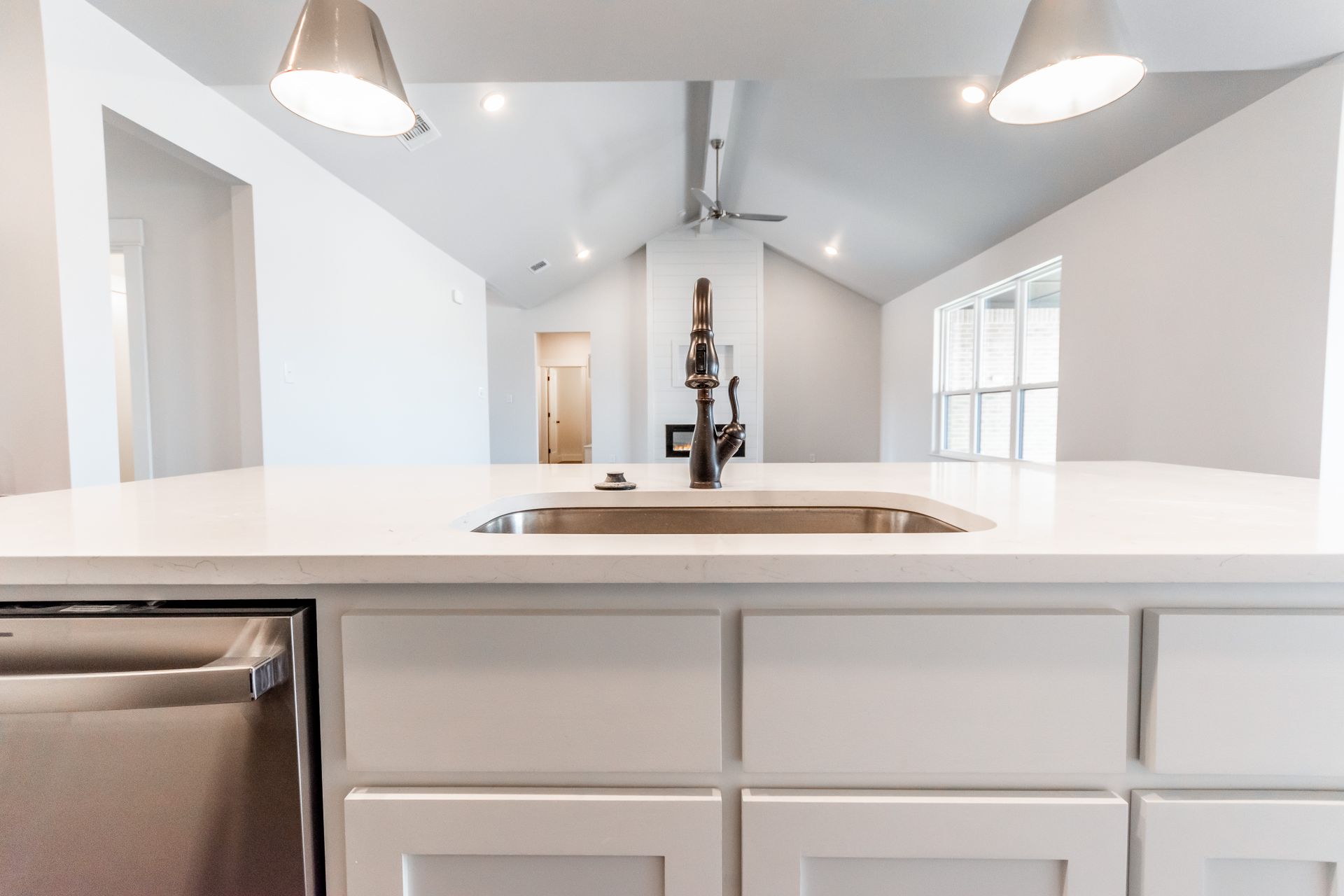 White kitchen with island and sink, pendant lights, and stainless steel dishwasher.