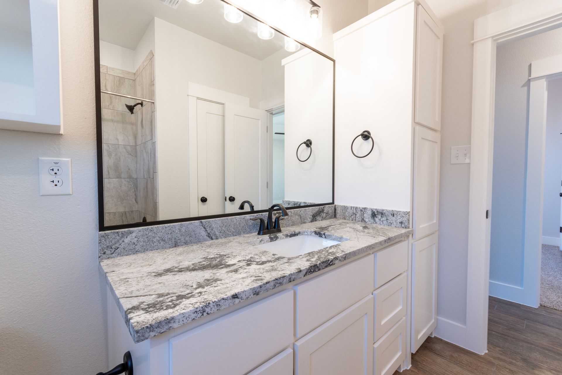 White bathroom vanity with granite countertop, mirror, and cabinet.