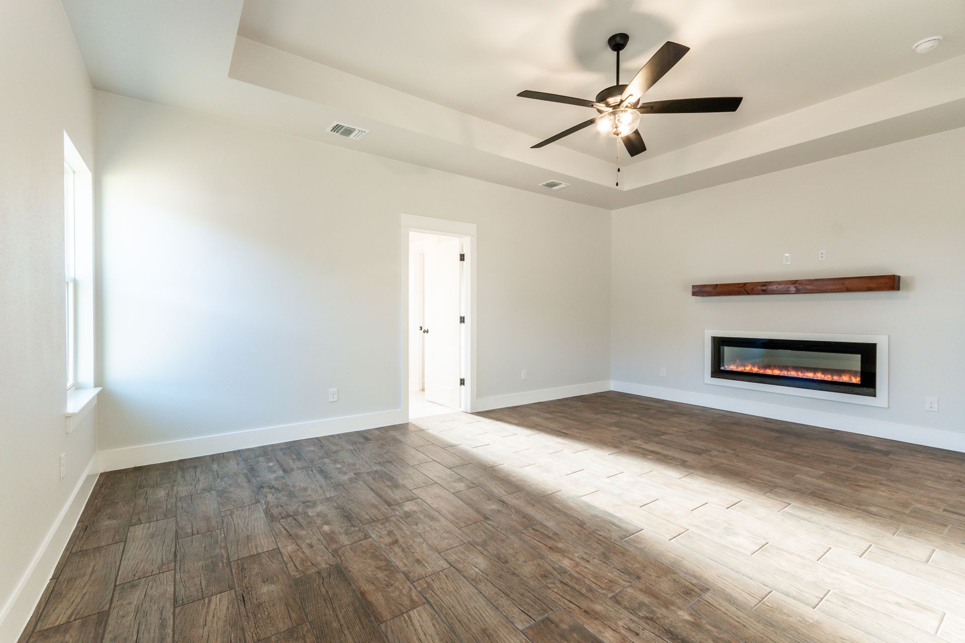 Empty living room with wood floors, fireplace, and ceiling fan.