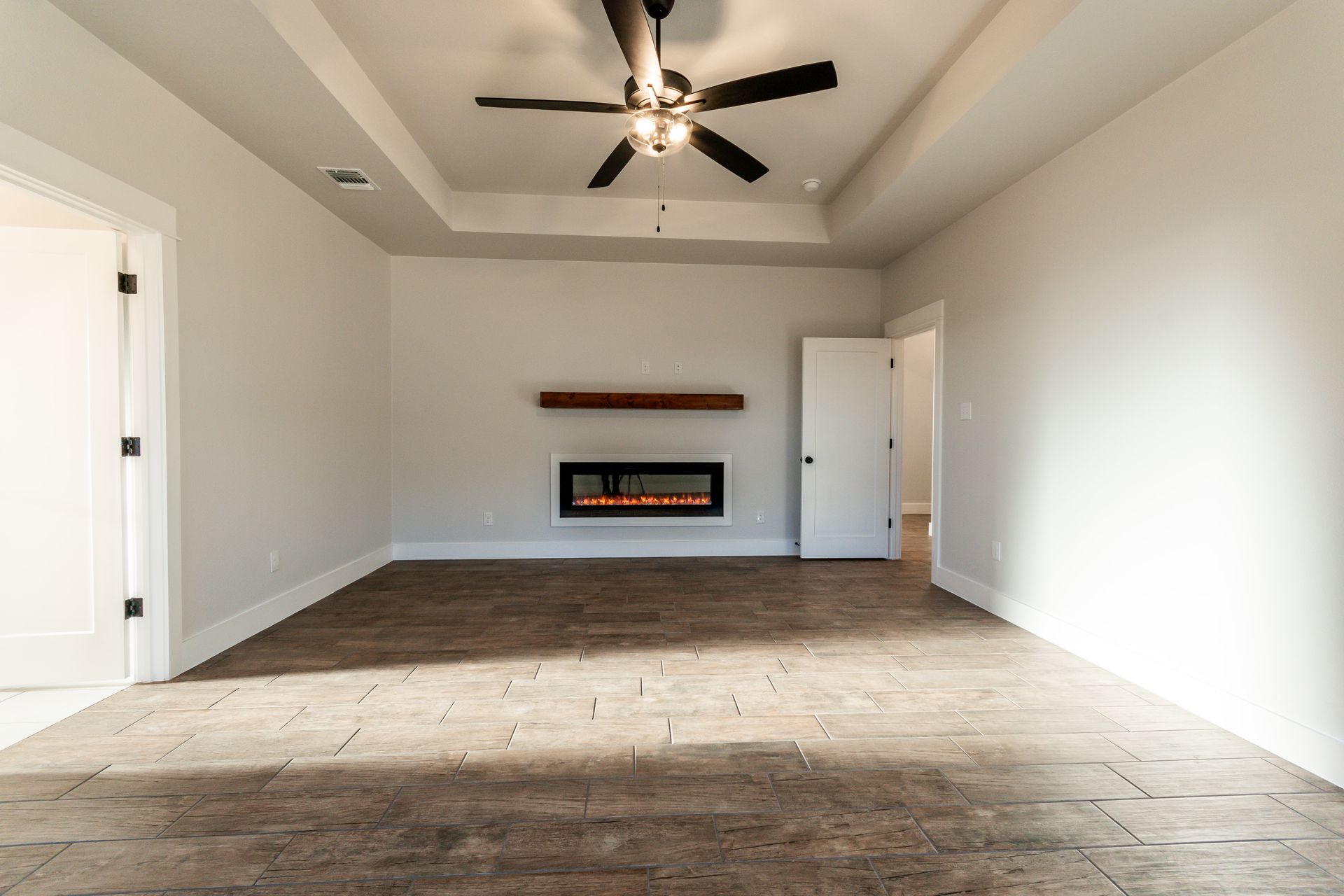 Empty modern bedroom with fireplace, ceiling fan, and hardwood floor.