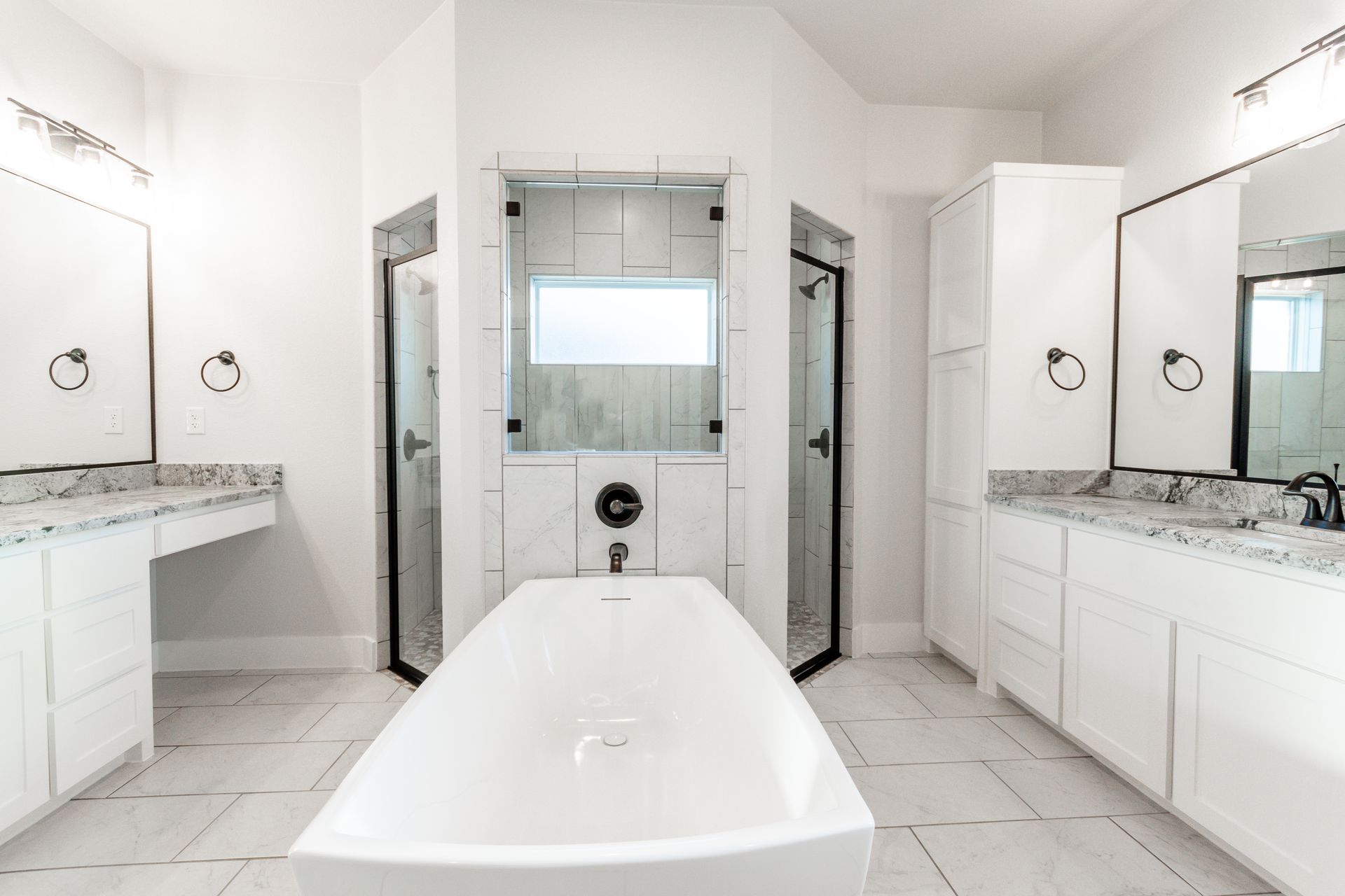Modern white bathroom with a tub, two vanities, and two glass door showers.