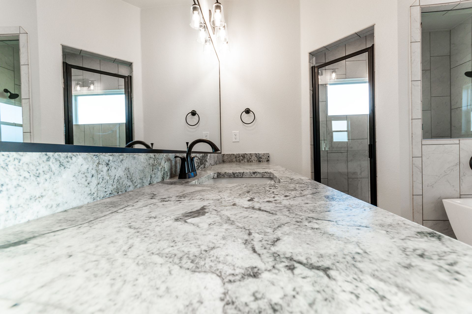 Bathroom with granite countertop, black fixtures, and a shower with a black frame.