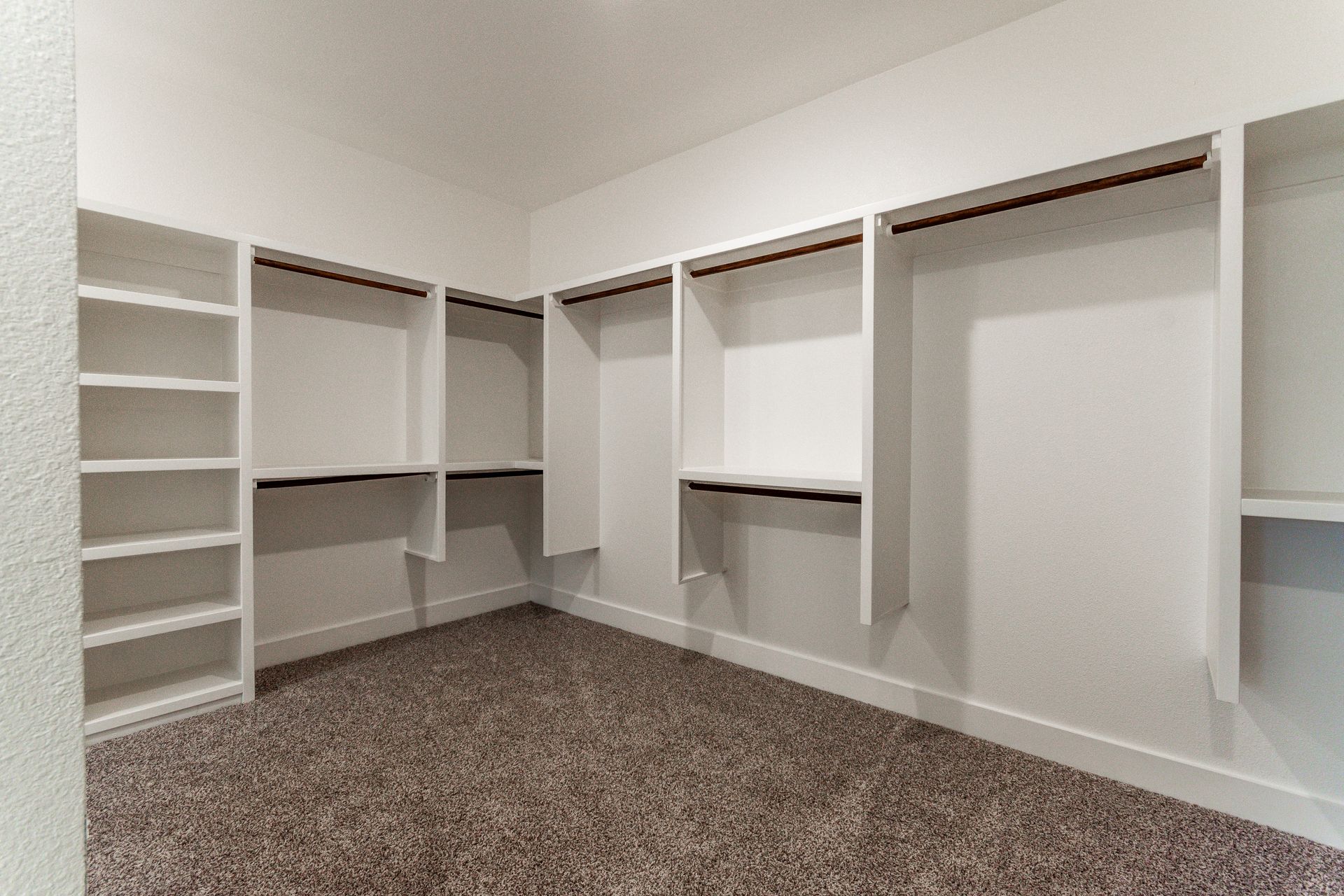 Empty white walk-in closet with shelves, hanging rods, and carpet flooring.