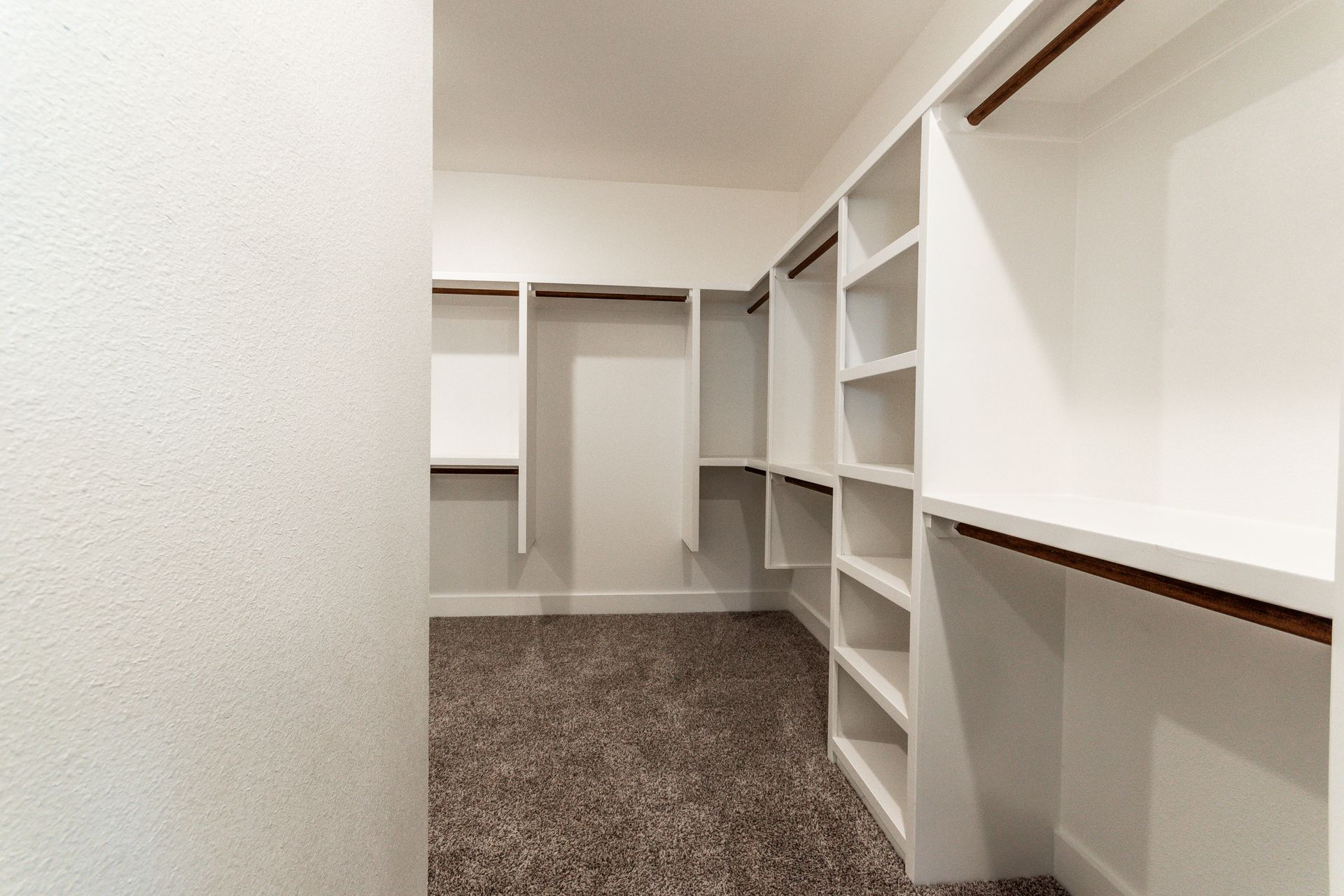 Empty walk-in closet with white shelves and a brown carpet.
