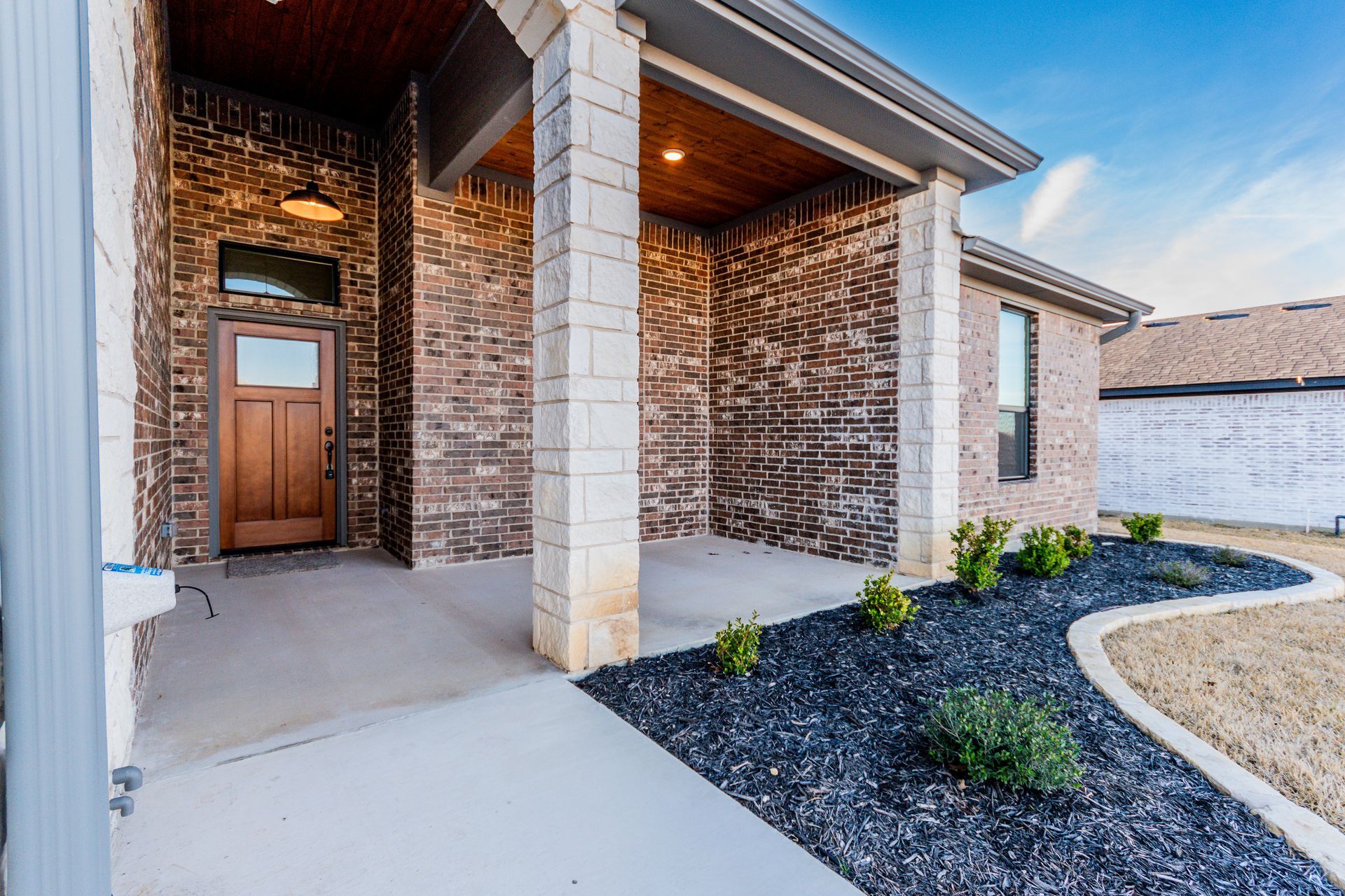 Exterior of a house with brick and stone accents, covered porch, and landscaped bed with black mulch.