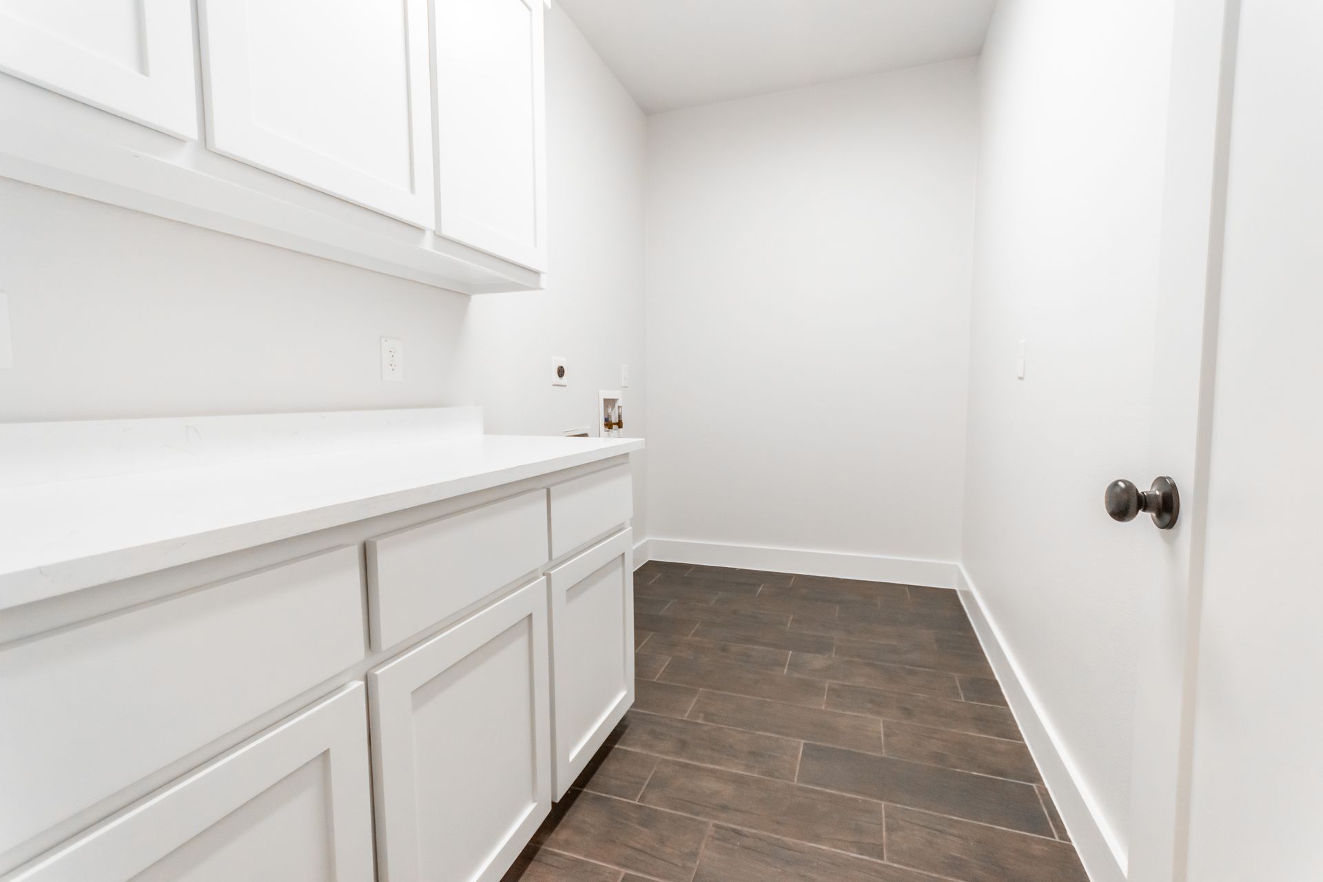 White laundry room with cabinets, counter, and dark tile floor.