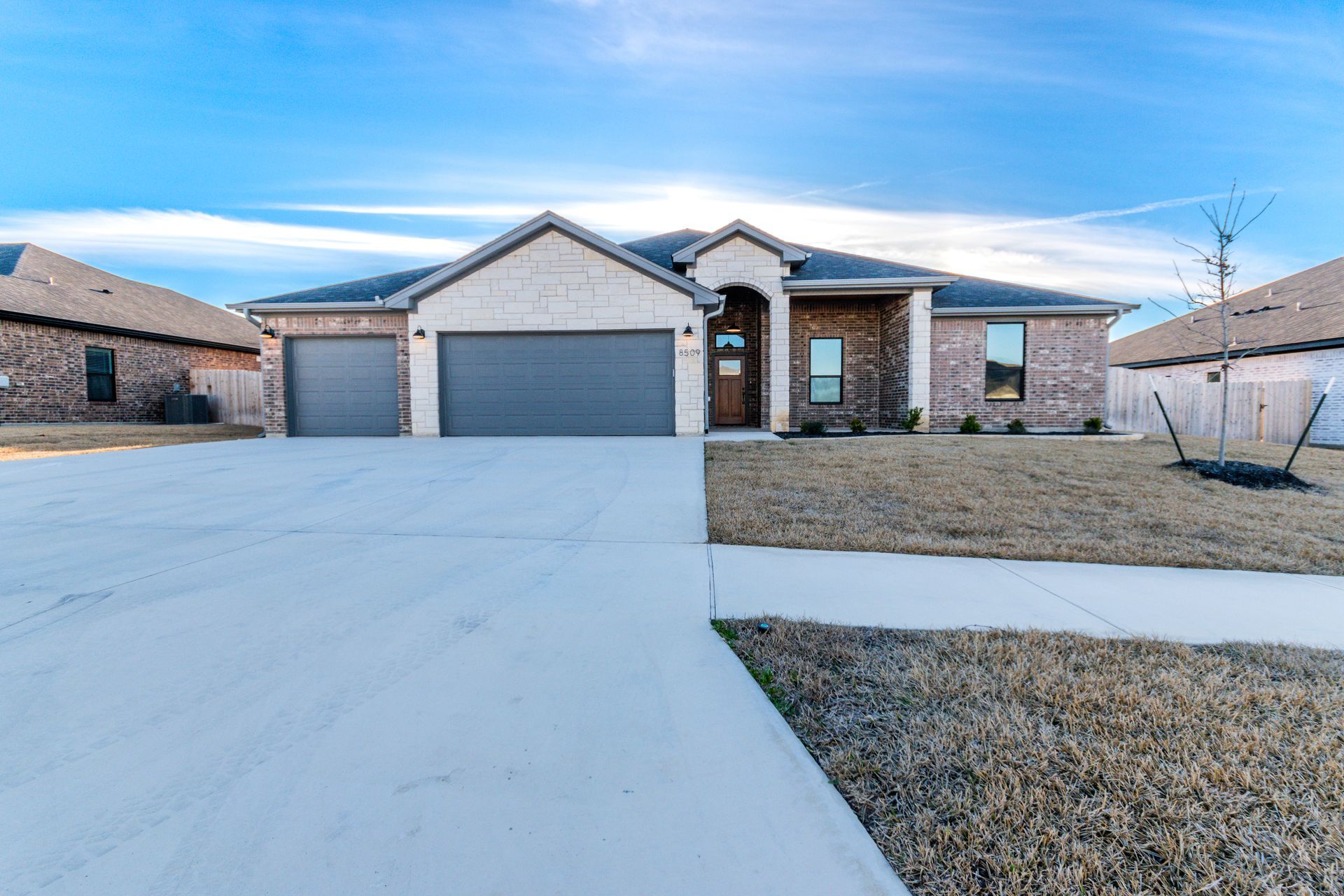 A single-story brick house with a three-car garage and a concrete driveway on a sunny day.