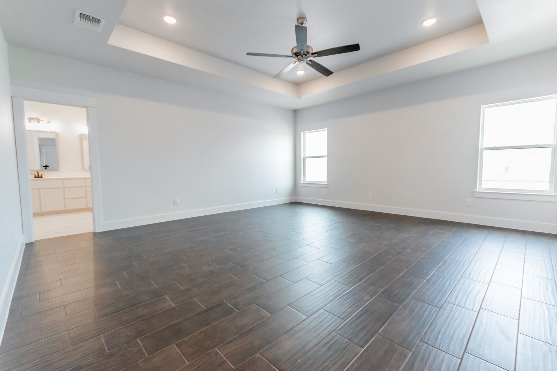 Empty modern bedroom with dark wood-look floor, white walls, and a ceiling fan.