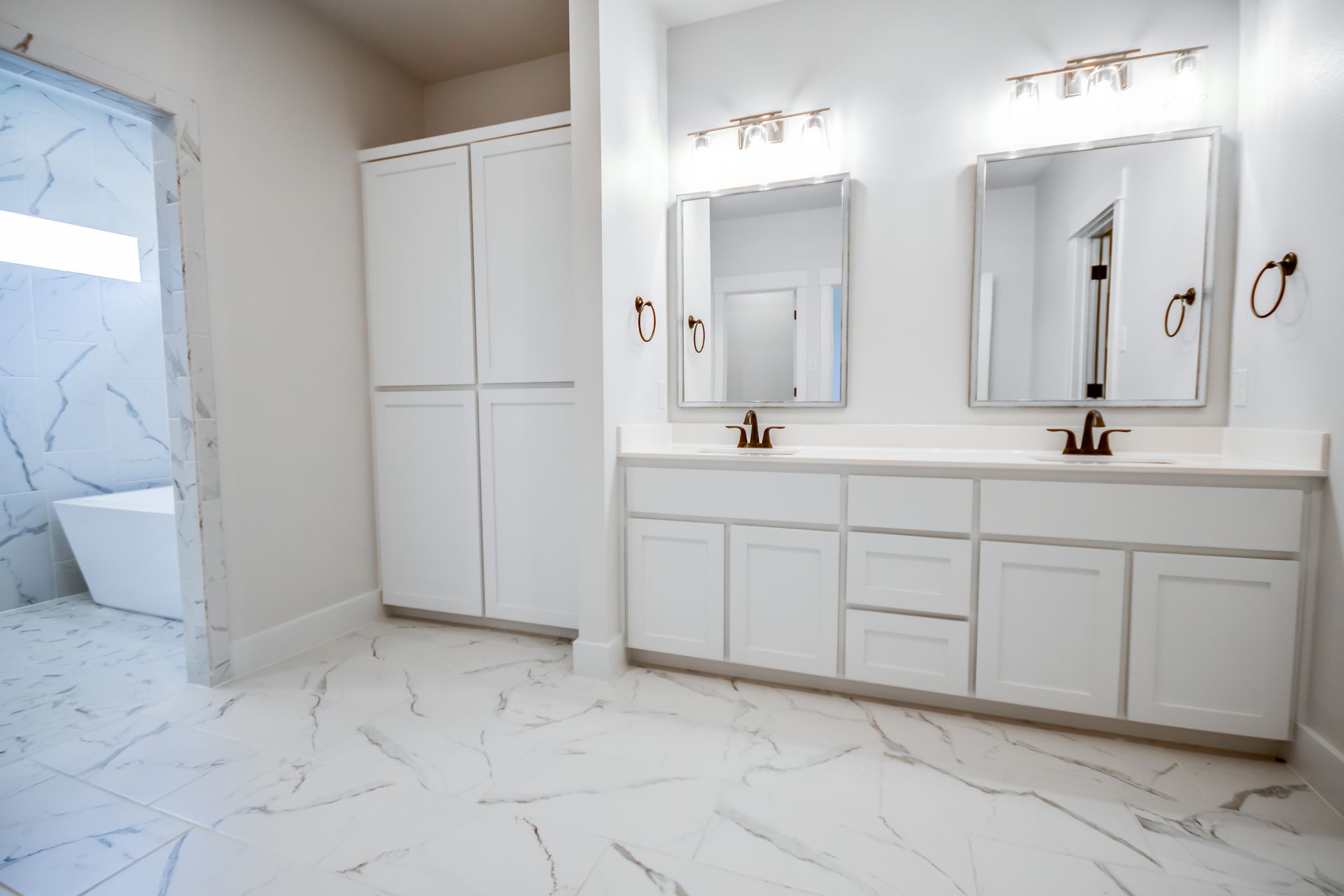 Spacious white bathroom with double vanity, tall storage cabinet, and large-tiled floors.